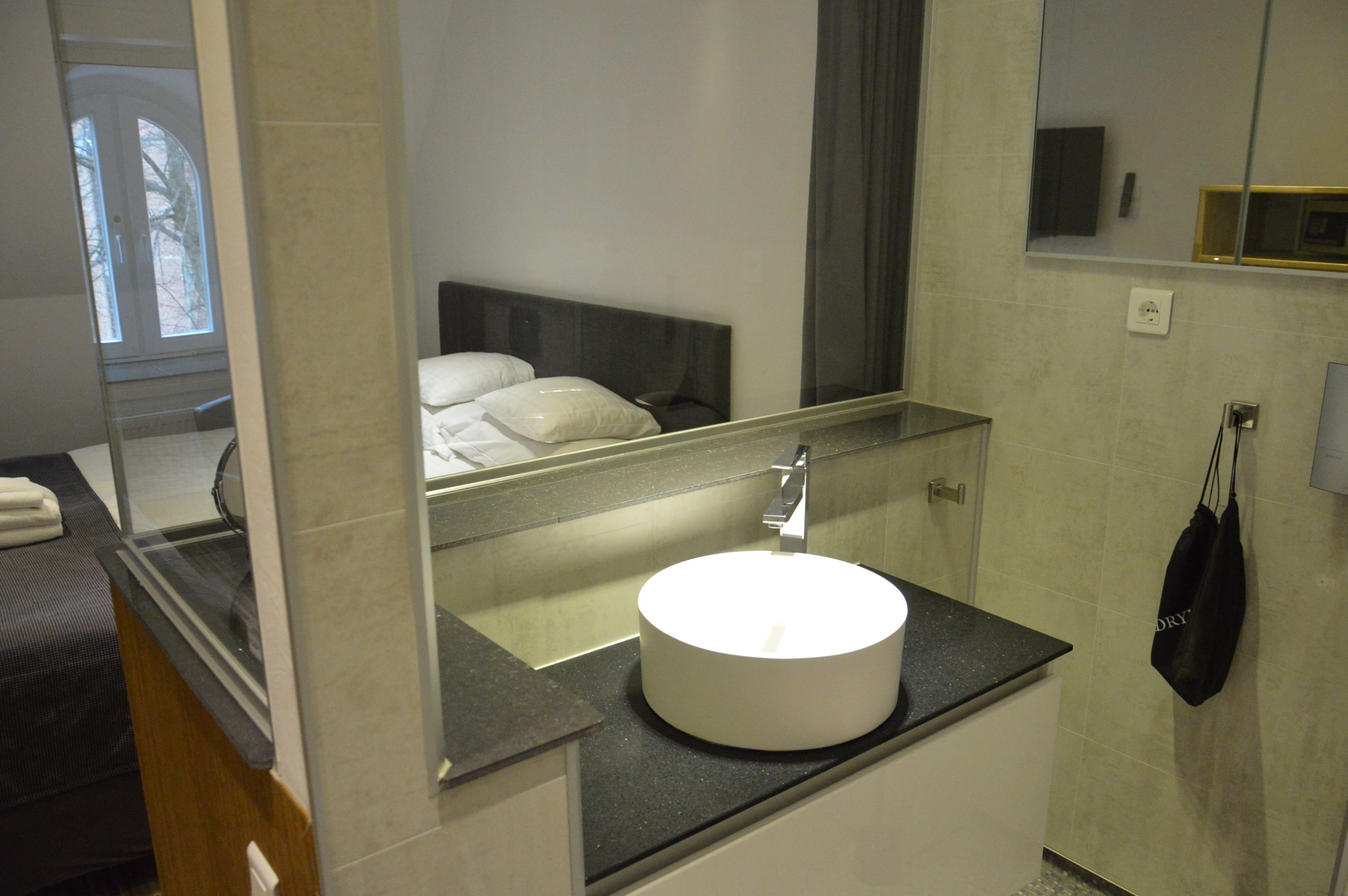 A bathroom with a round white sink, a mirror, and a towel rack.