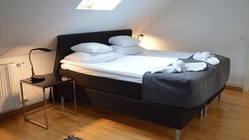 Un dormitorio moderno con tragaluz, una cama con ropa de cama blanca, una mesita de noche con lámpara y una pequeña alfombra.