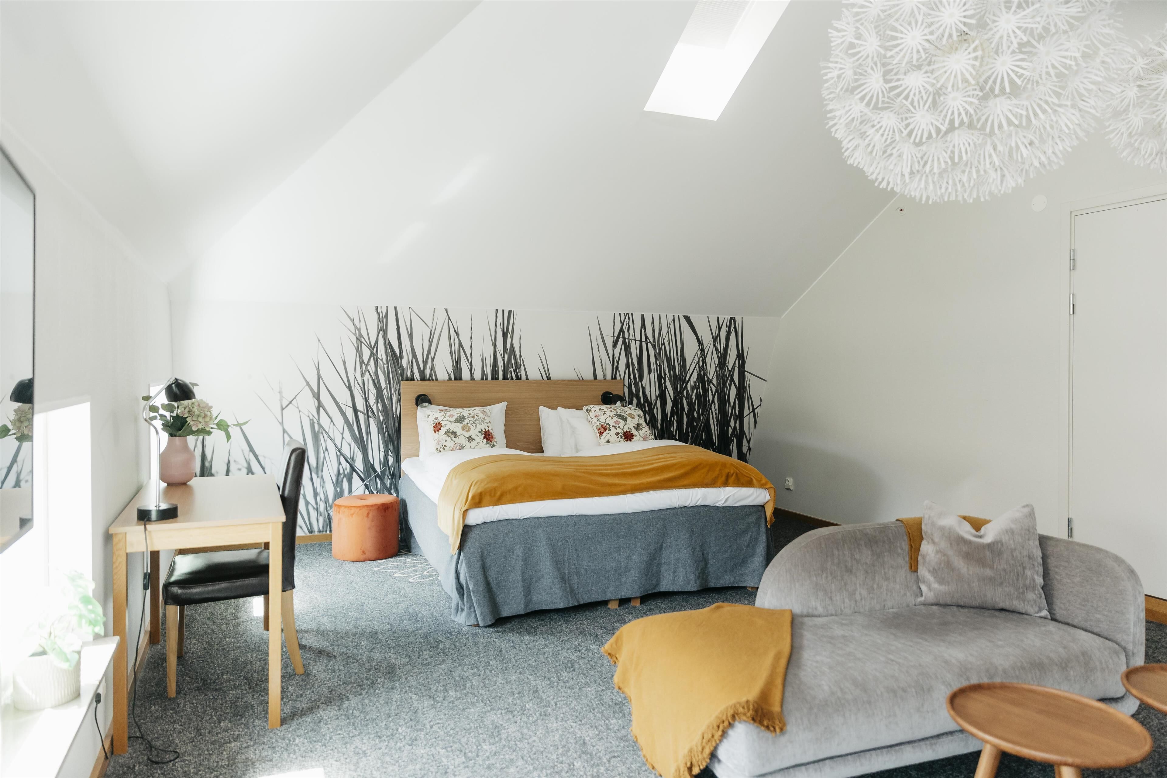 A modern bedroom with a bed, a desk, a sofa, and a unique ceiling light fixture.