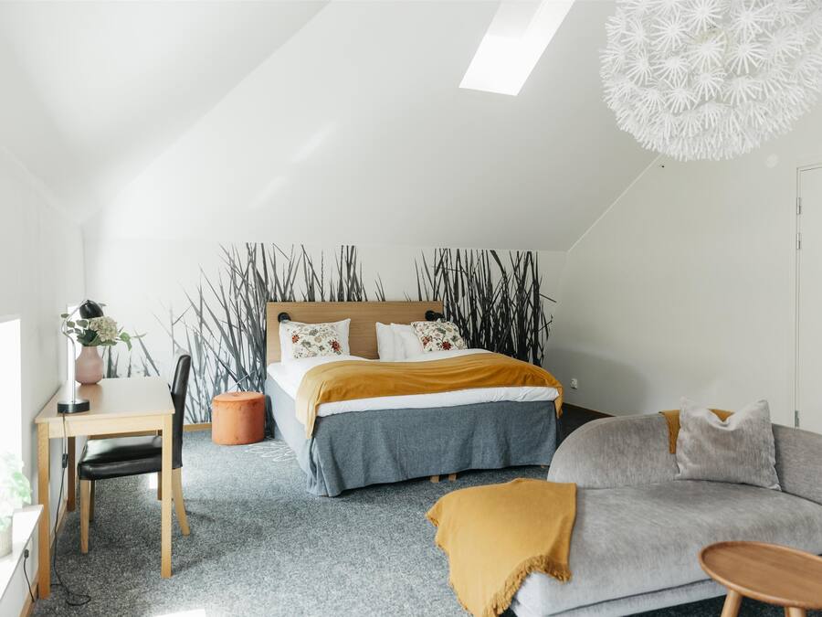 A modern bedroom with a bed, a desk, a sofa, and a unique ceiling light fixture.