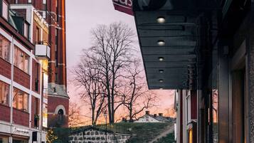 A building with a red brick tower, a flag with "BW Bestester PLUS" text, and a street with cars and a pedestrian.