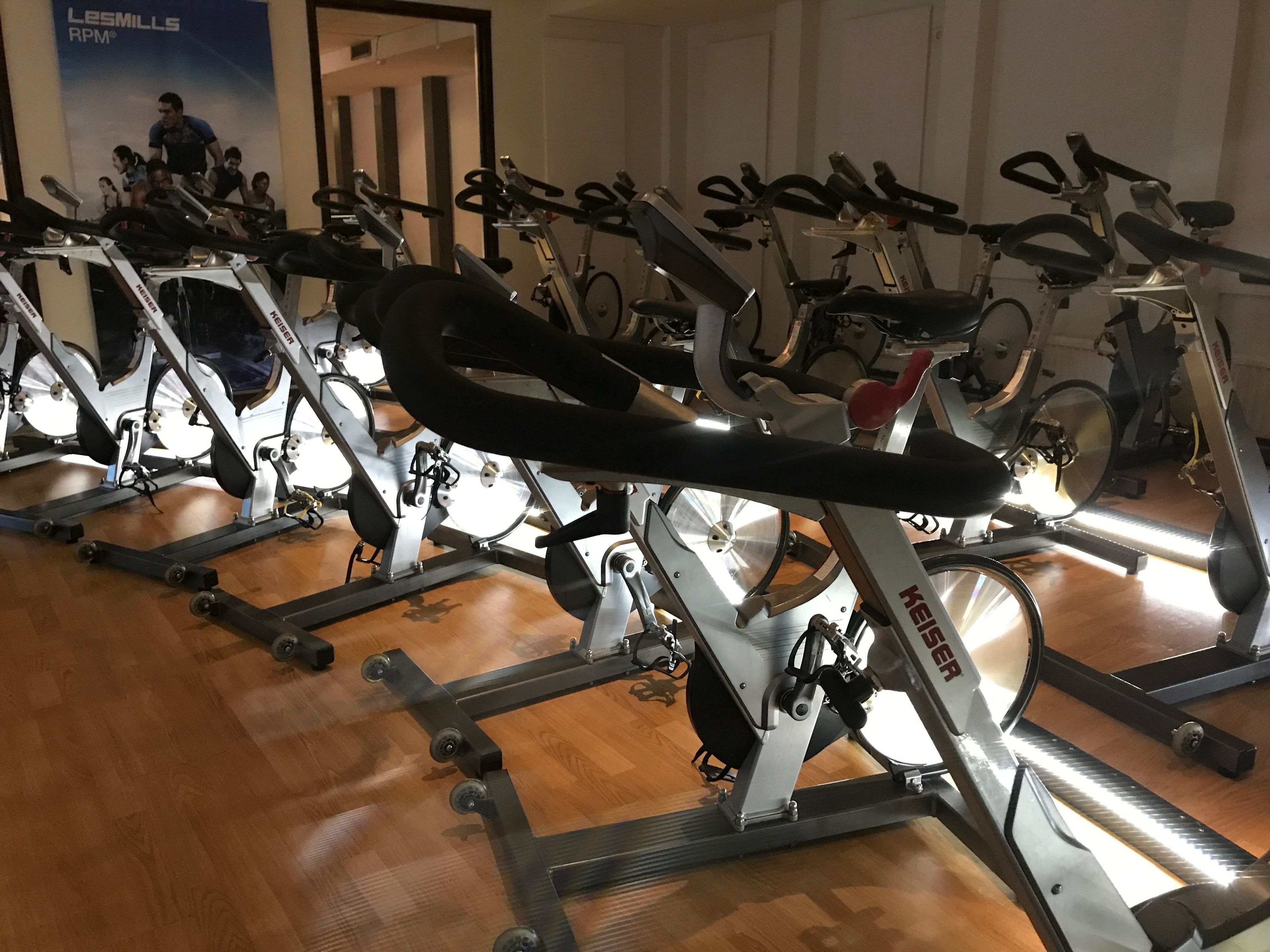 A row of stationary bikes in a gym with wooden flooring.