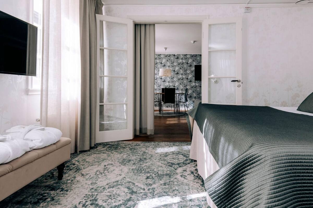 A hotel room with a bed, a sofa, a television, and a bathroom visible through an open door.