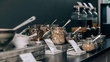 Un mostrador de autoservicio con diferentes alimentos en recipientes de vidrio, cada uno con una cuchara y etiqueta de precio.
