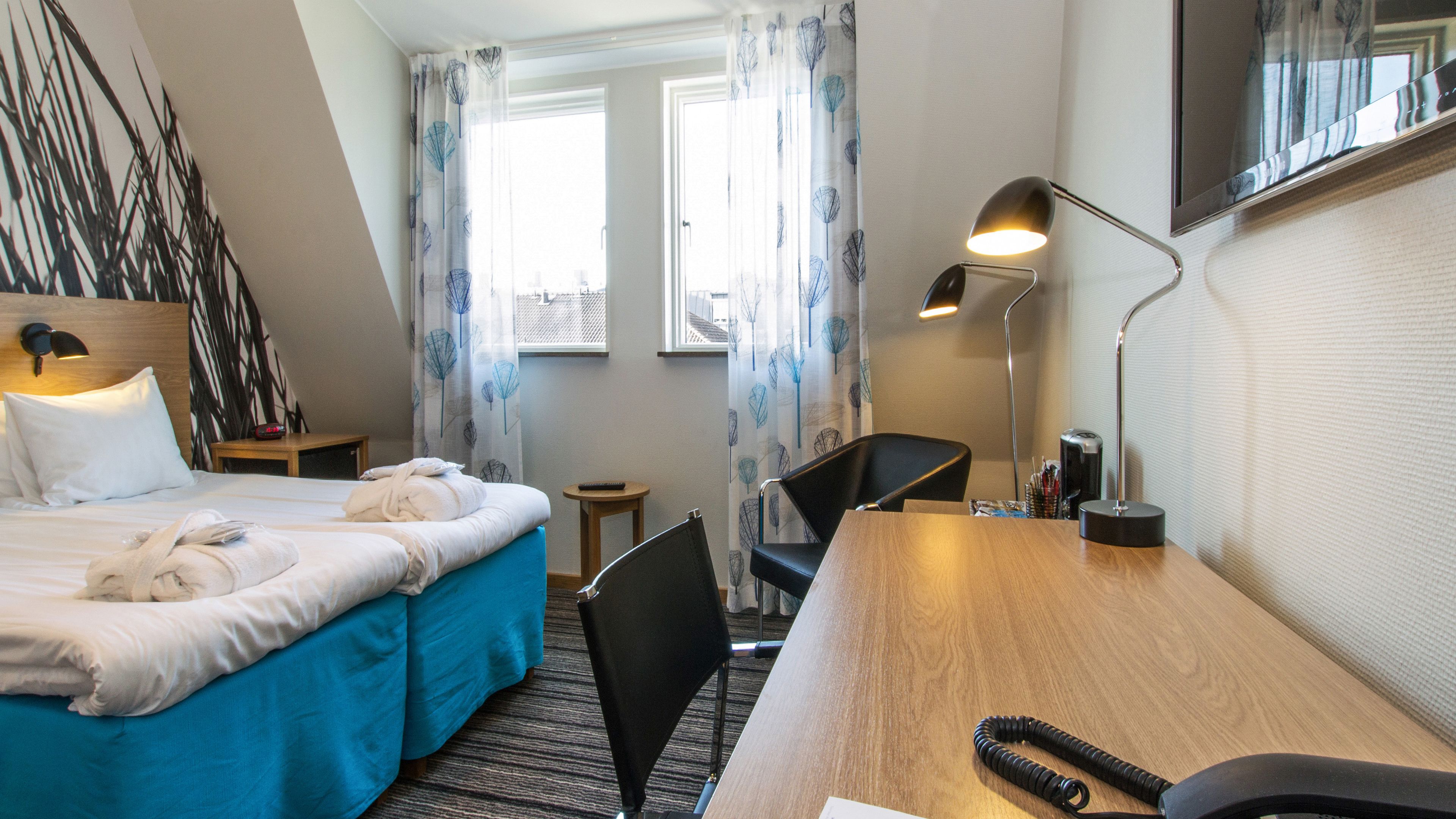 A hotel room with two beds, a desk, a chair, a lamp, and a TV.
