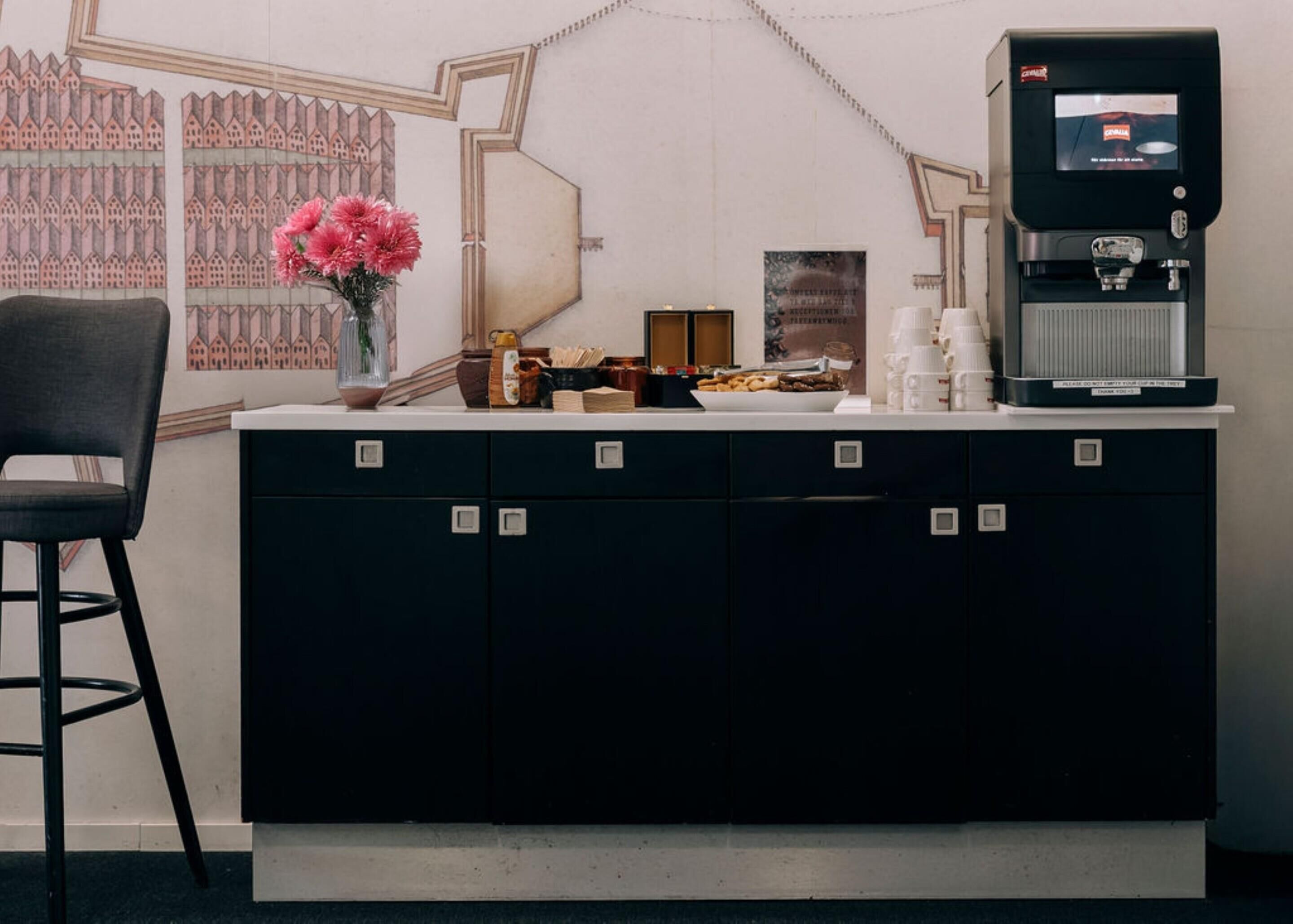 A counter with a coffee machine, a vase with flowers, and a chair.