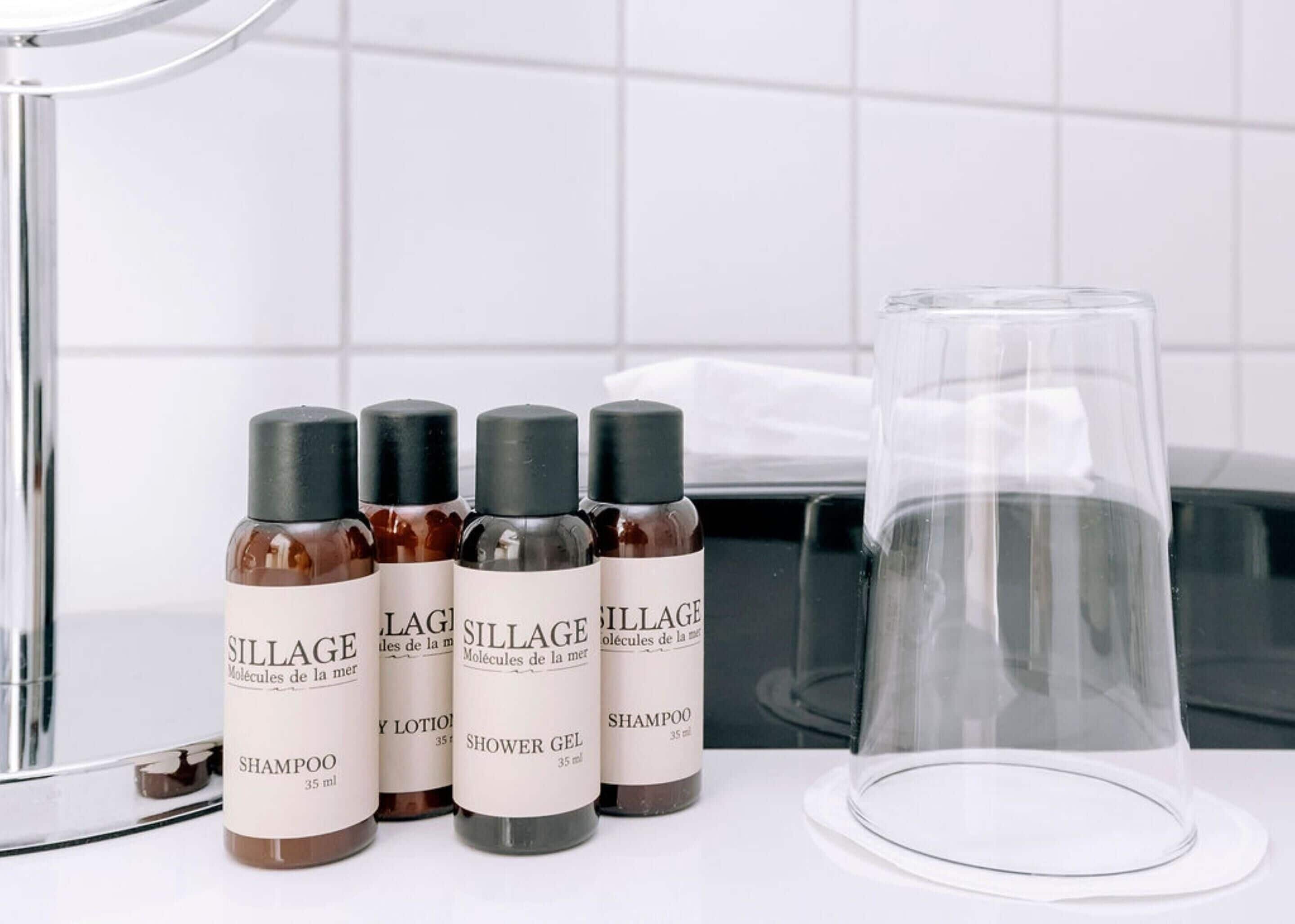 Fyra flaskor med hårvårdsprodukter från Sillage och en genomskinlig glasbehållare på en vit yta.