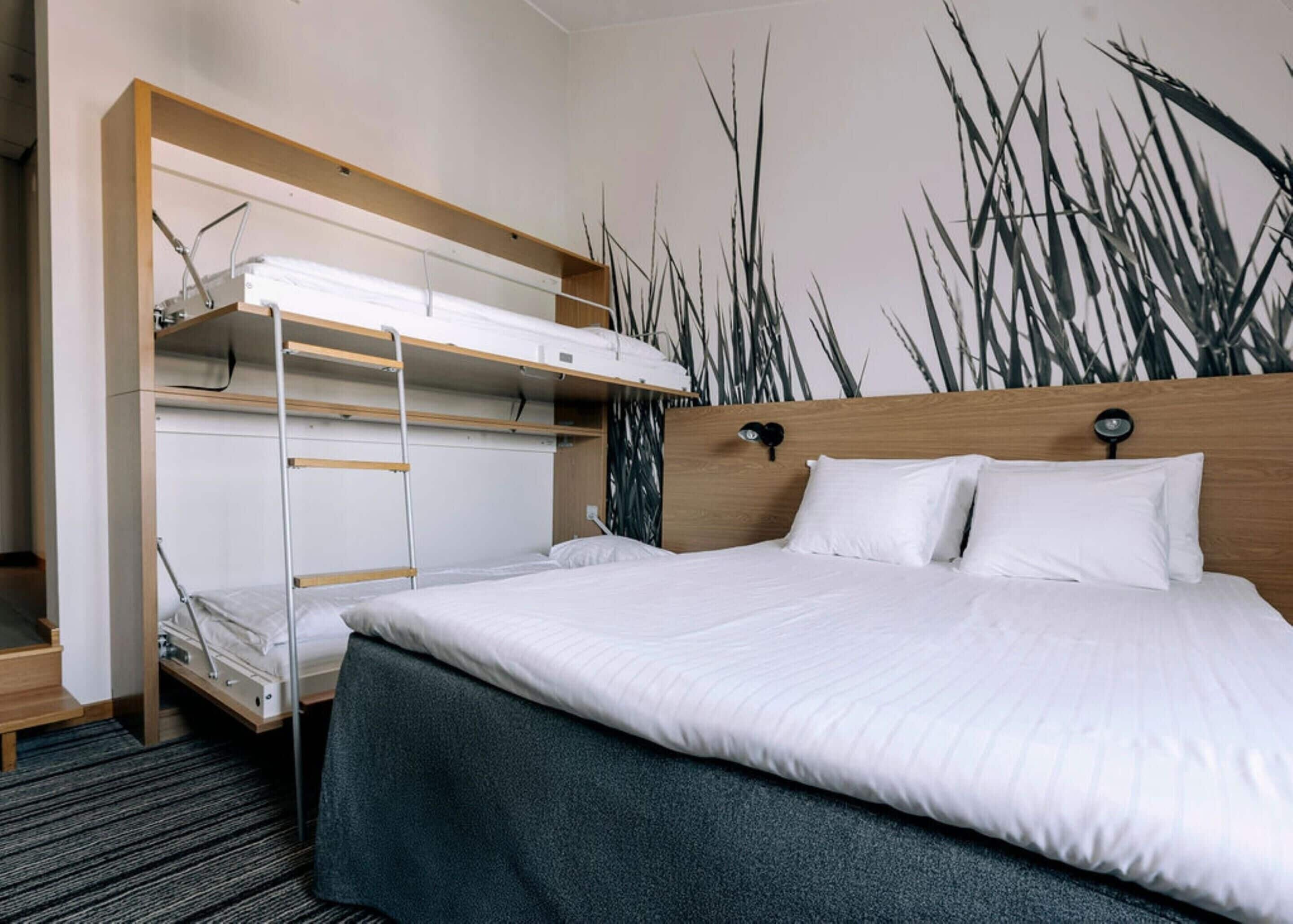 Habitación de hotel con literas, cabecera de madera y un mural de pastos altos.