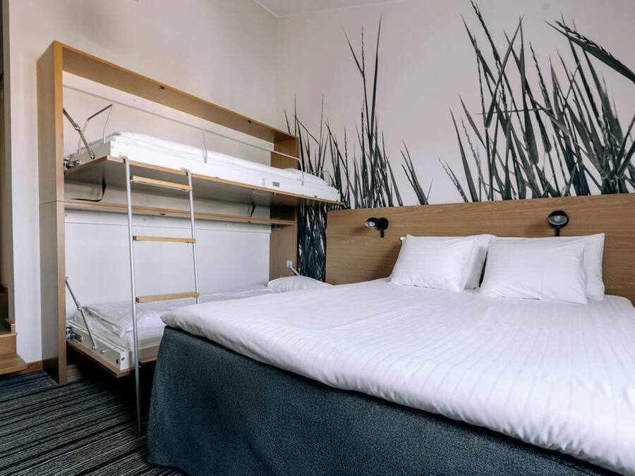 Habitación de hotel con literas, cabecera de madera y un mural de pastos altos.