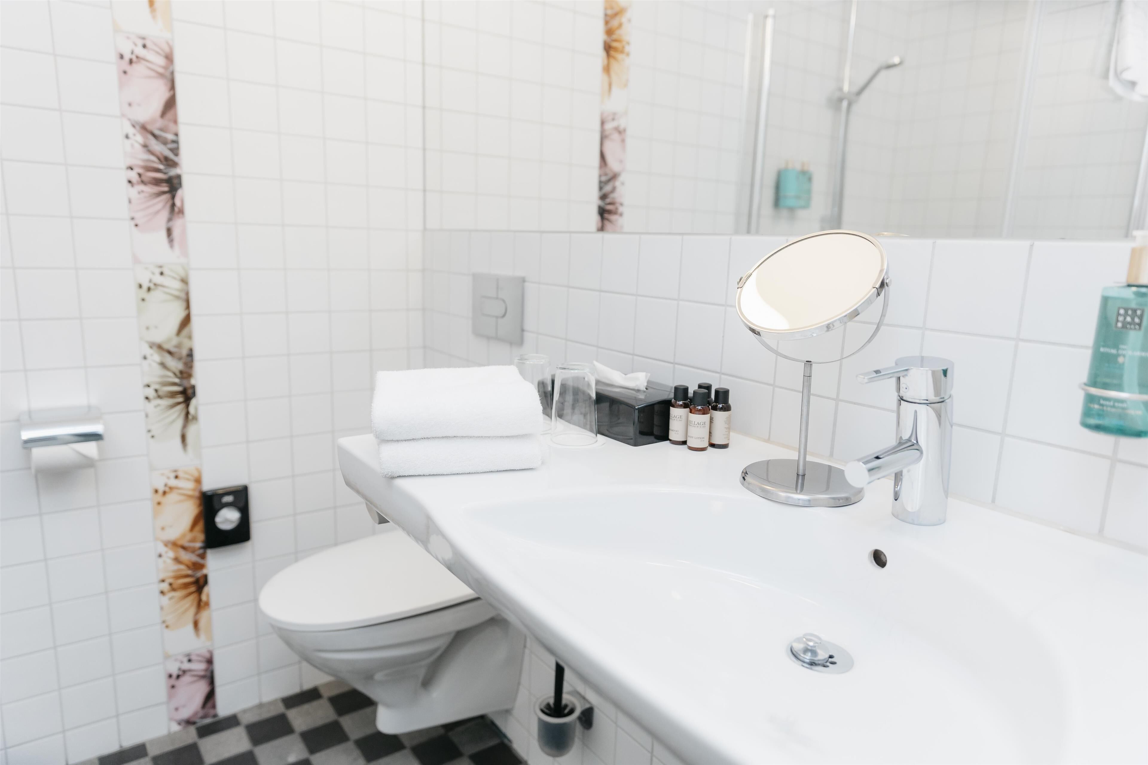 Un baño moderno con un lavamanos, espejo y retrete blancos.