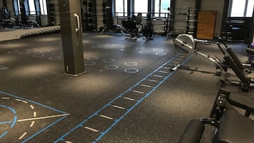 Een sportschool met trainingsapparatuur, rekken voor gewichten en een digitale klok waarop 8:40 staat.