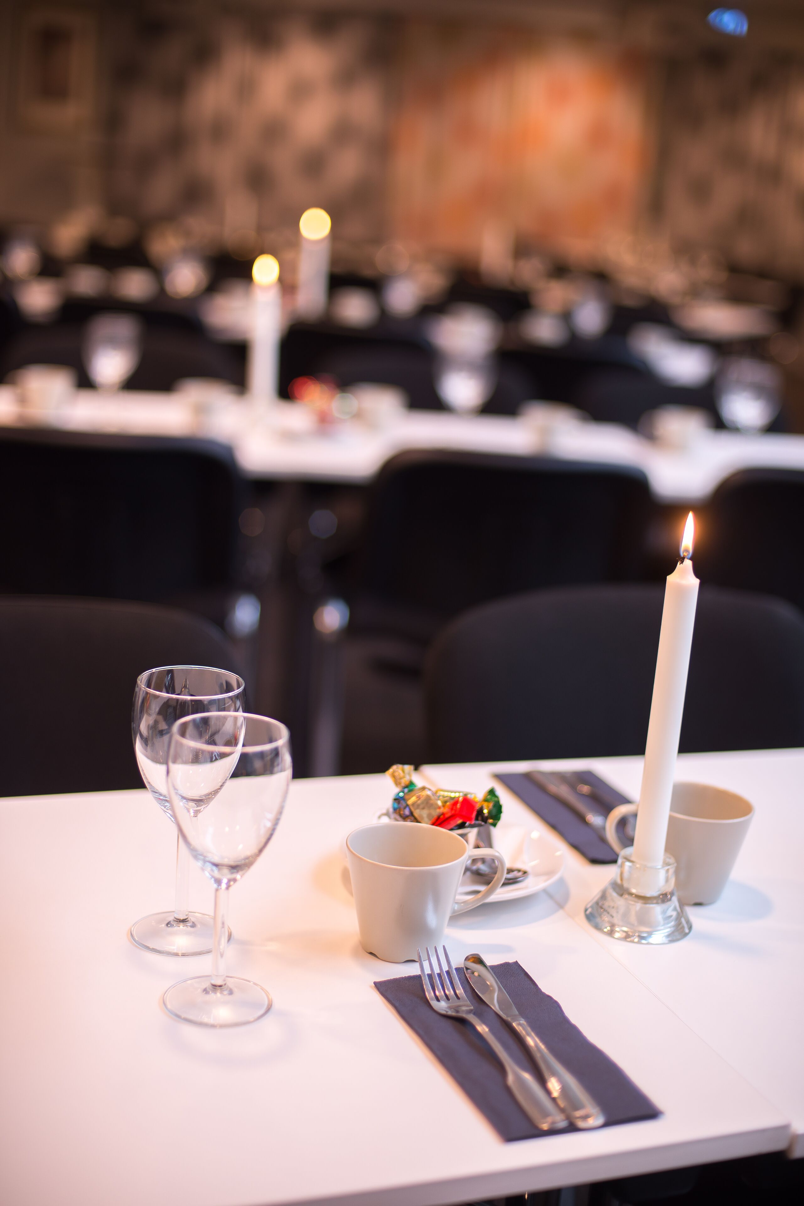 A dining table set with wine glasses, a candle, and cutlery.