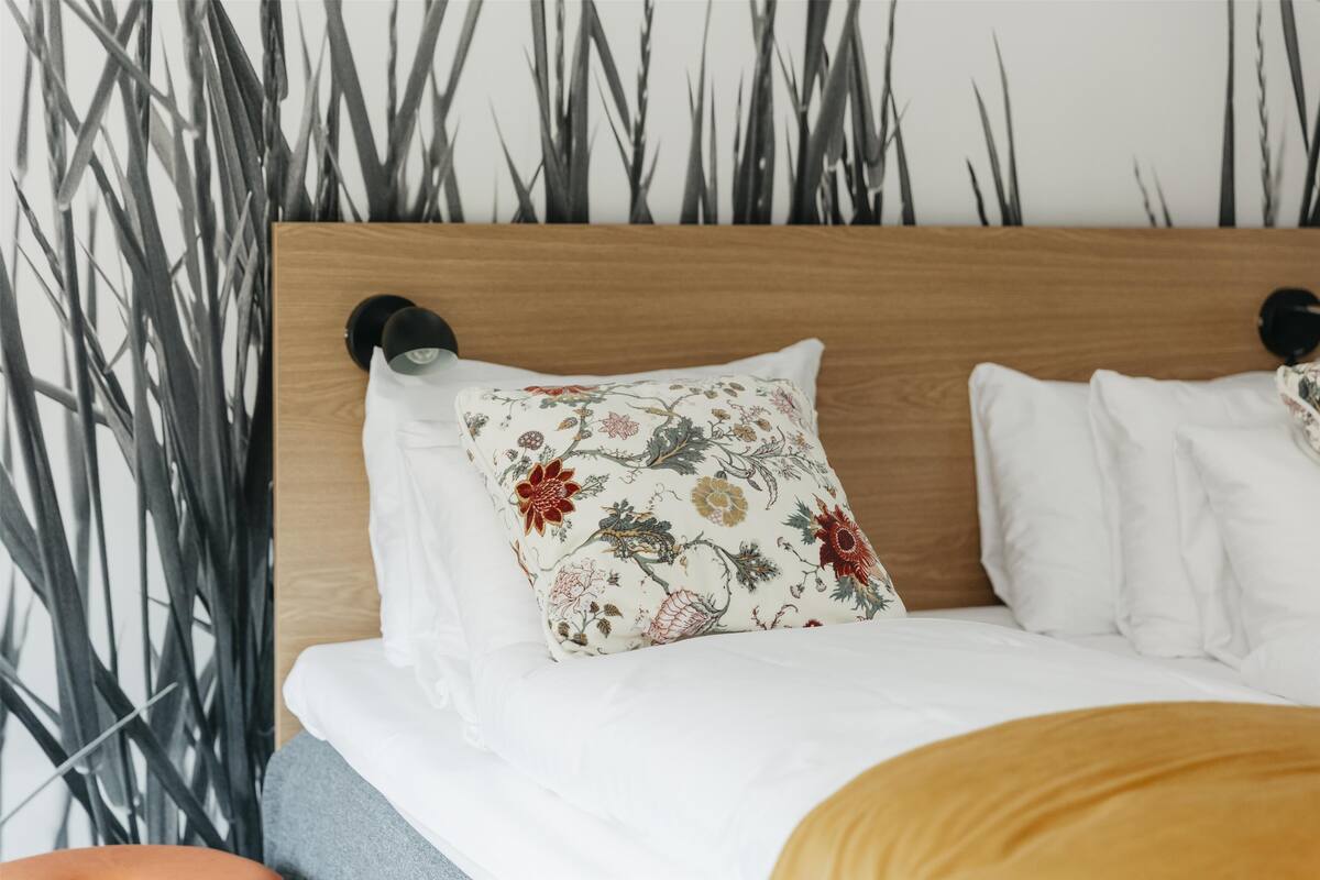 A bed with a wooden headboard, white bedding, and a floral pillow.