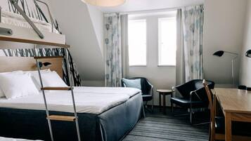 Ett hotellrum med en våningssäng, ett skrivbord, en stol och två fönster med gardiner.