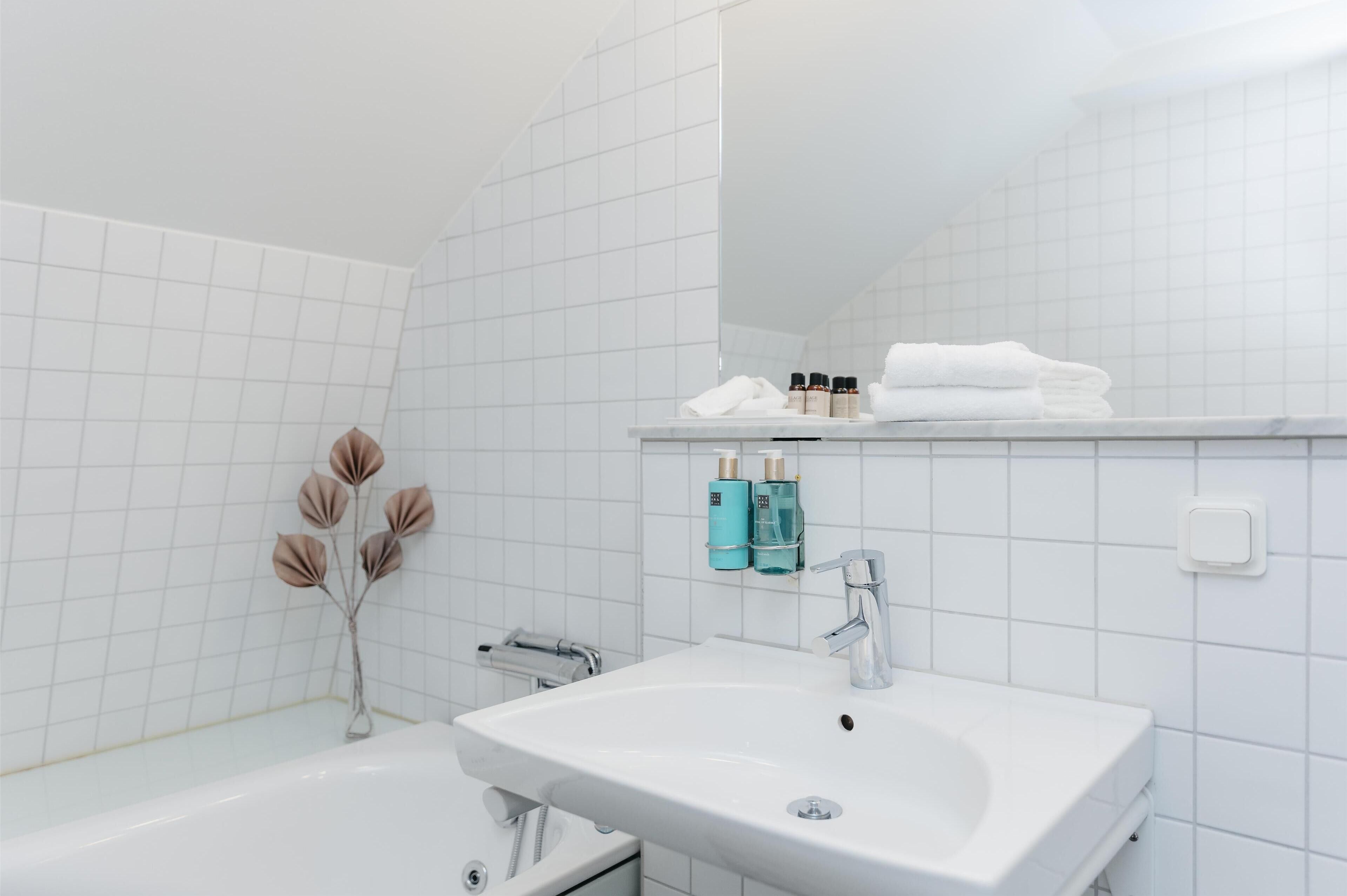 Ett badrum med ett vitt handfat, en spegel och en hylla med toalettartiklar.