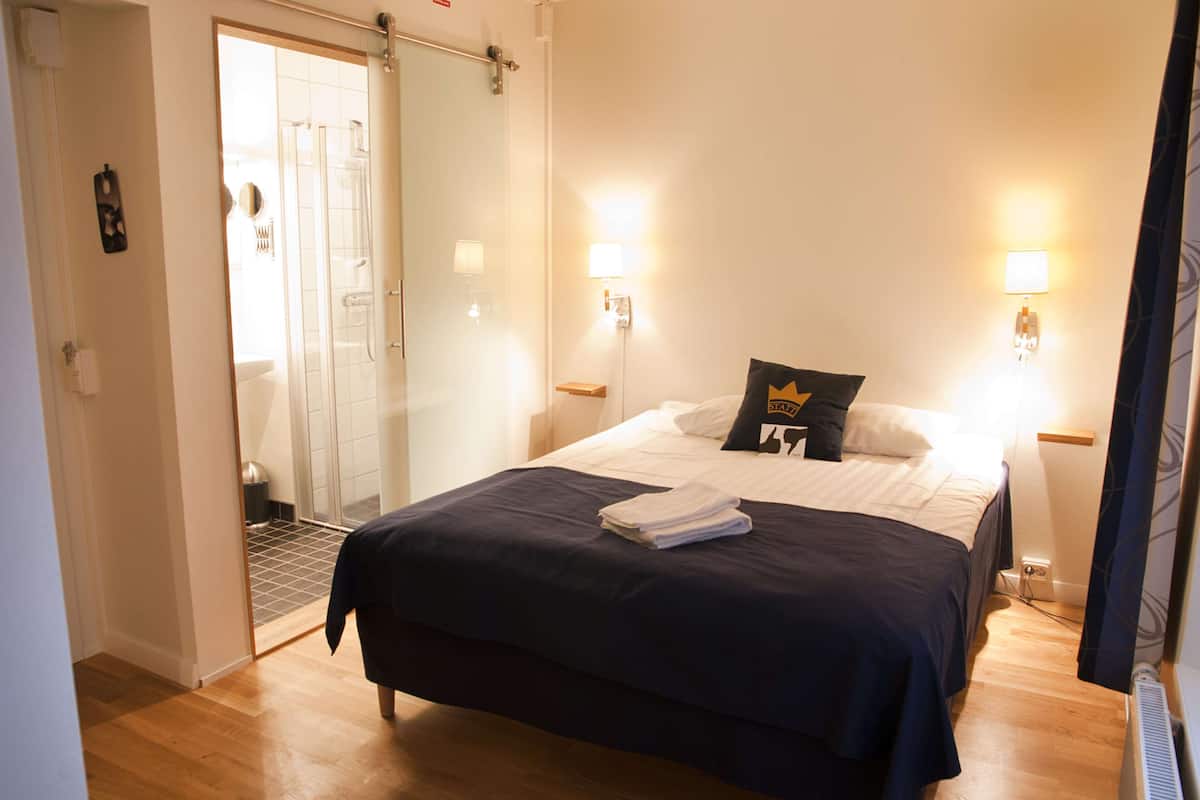 A hotel room with a bed, a shower, and two wall-mounted lights.