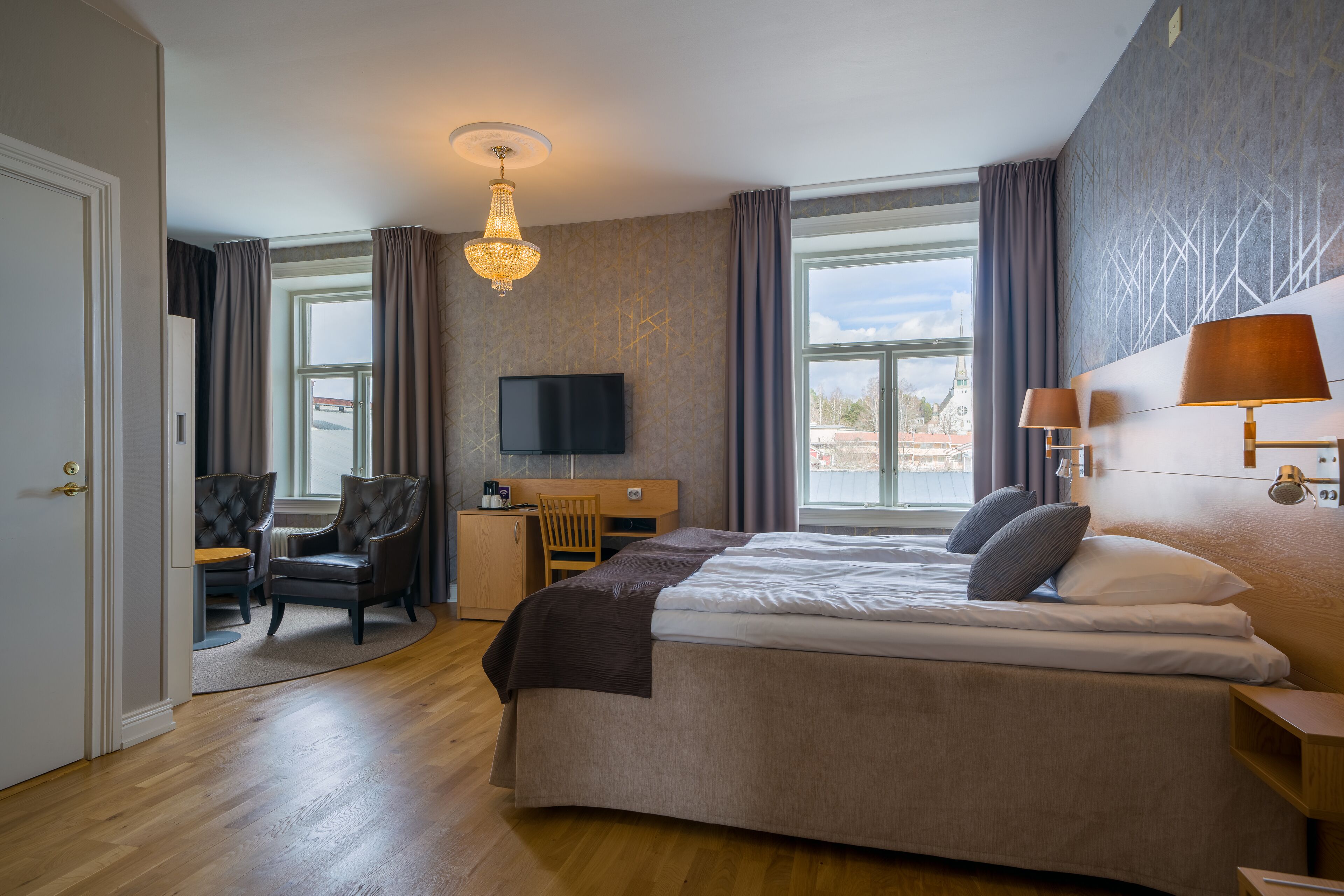 A hotel room with a large bed, a desk with a chair, a TV, and a window with curtains.