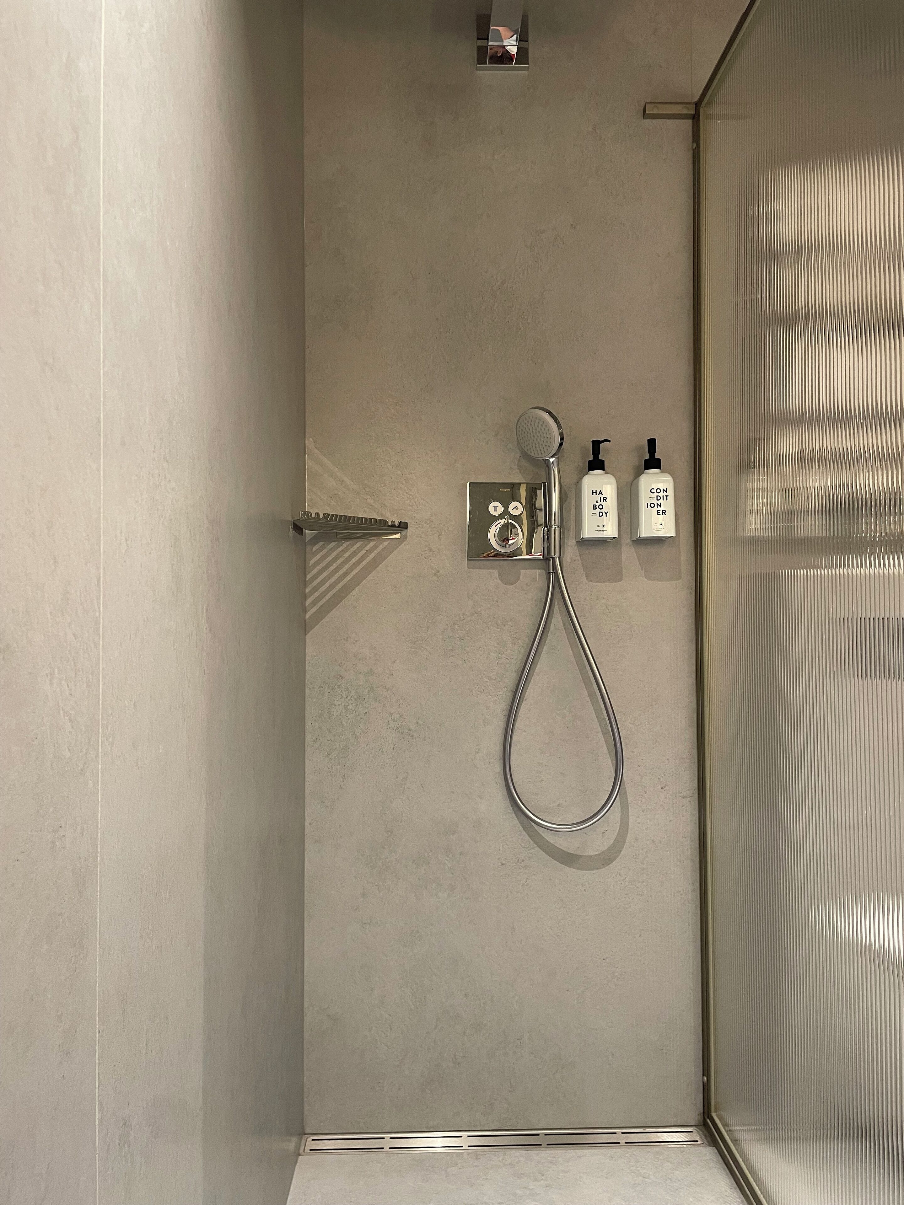 Un área de ducha moderna con un cabezal de ducha de mano, un panel de control y dos botellas de jabón para manos.