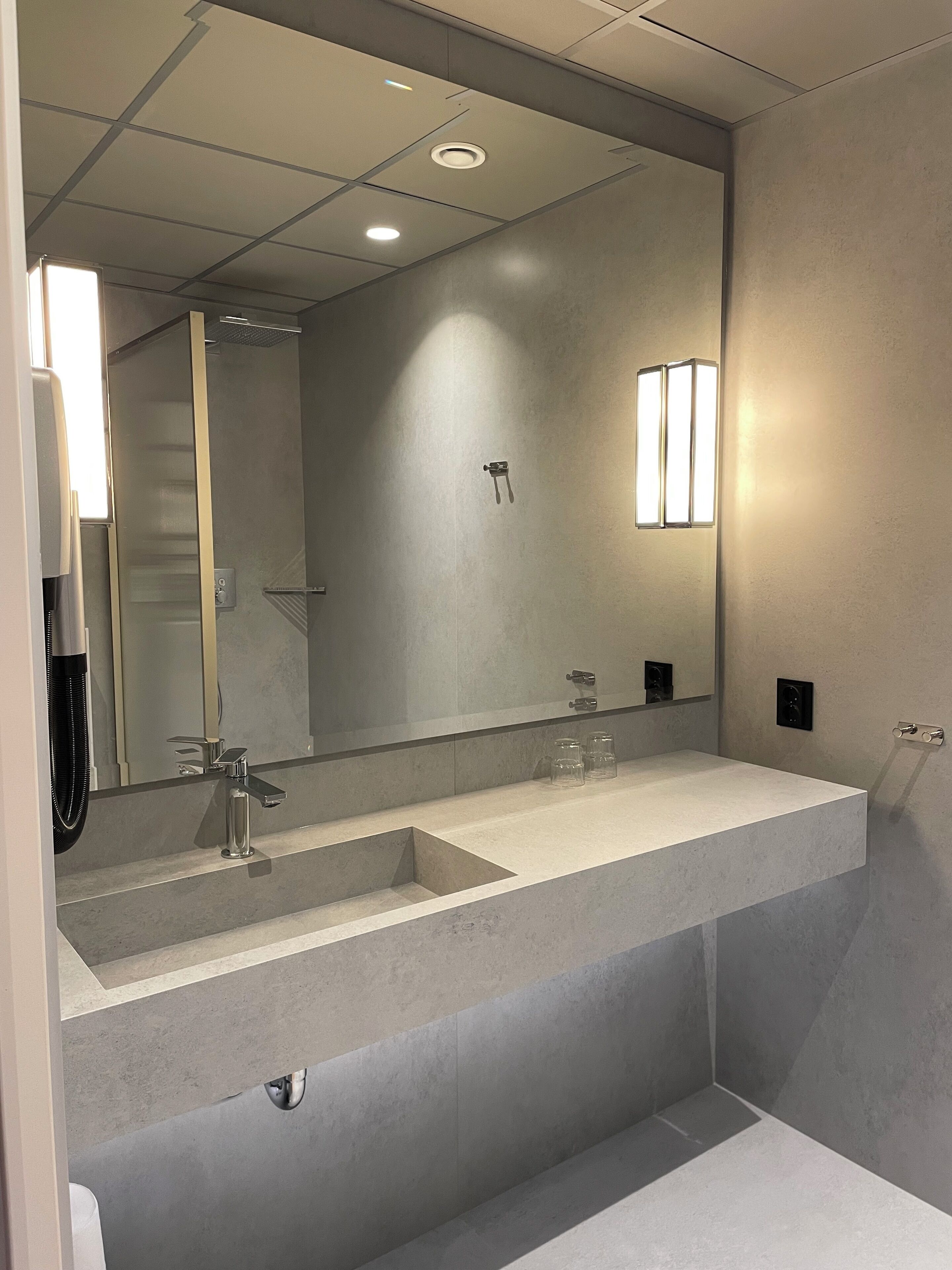 A modern bathroom with a large mirror, two sinks, and a shower.