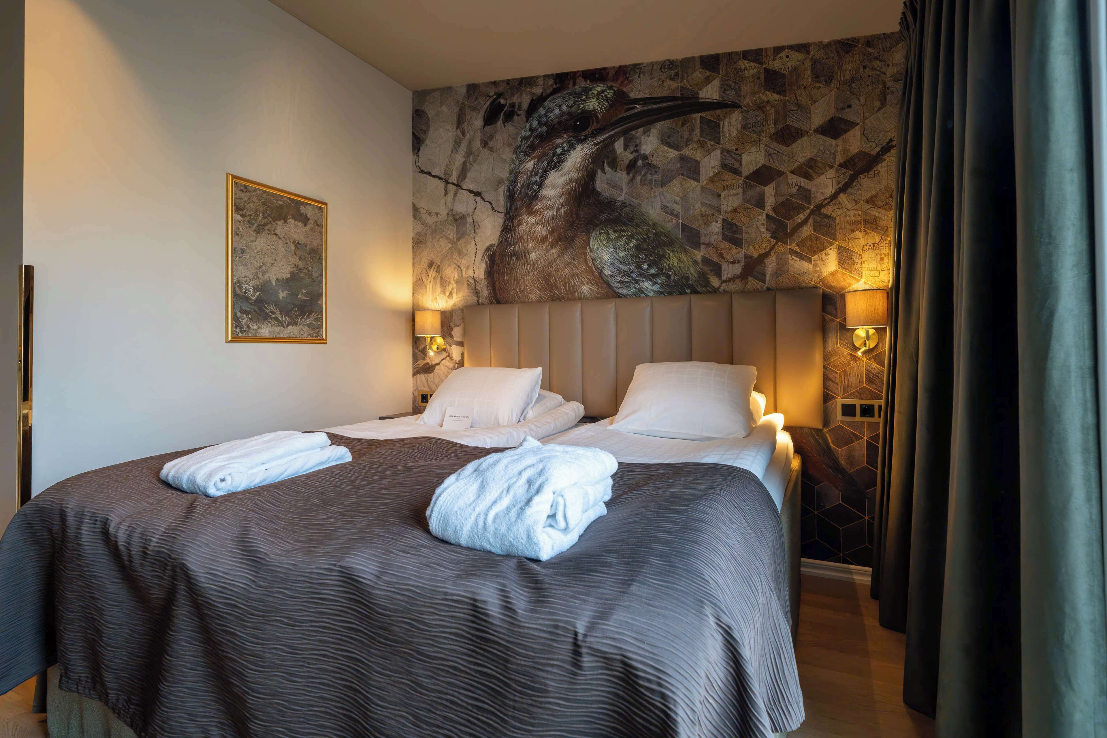 Habitación de hotel con una cama grande, dos lámparas de noche, un mural en la pared y un cuadro enmarcado.