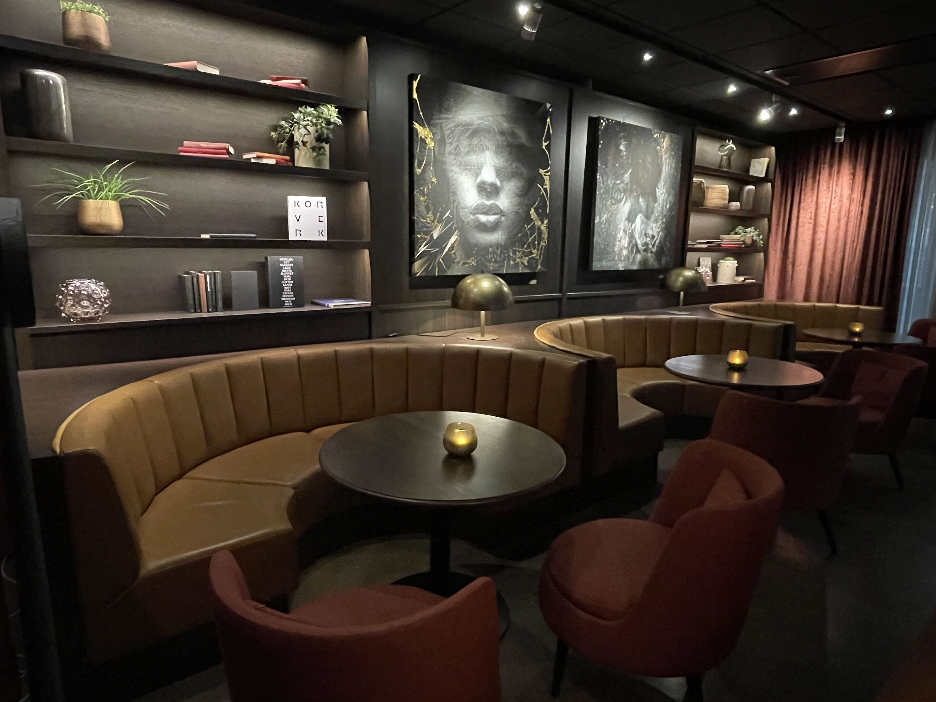 A modern lounge area with curved seating, small round tables, and decorative wall art.