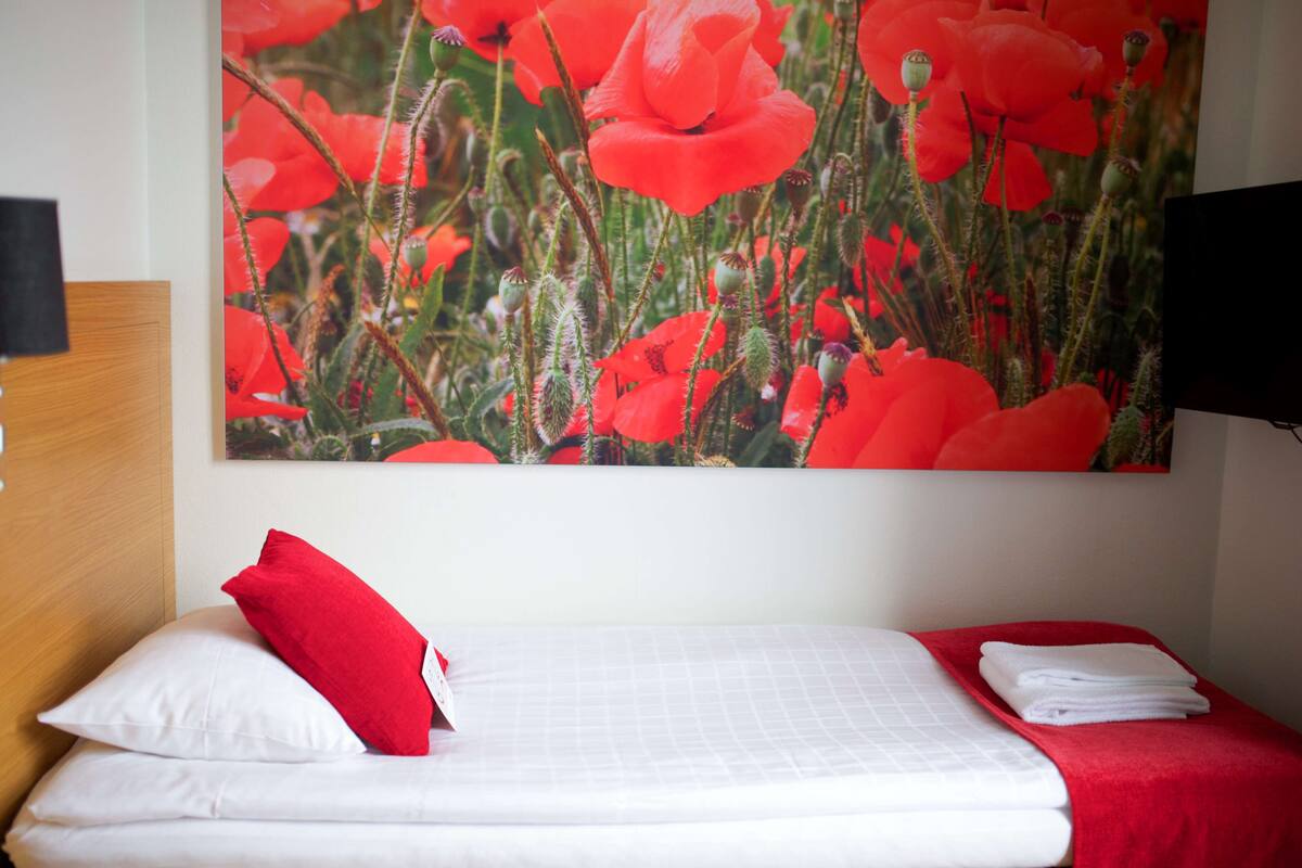A hotel room with a bed, white bedding, a red pillow, and a red blanket.