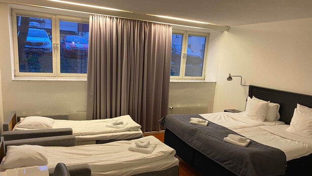 A hotel room with two single beds, a larger bed, a desk, and a chair. - Hotell Alfred Nobel (Karlskoga)