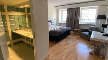 Et hotelværelse med seng, skrivebord, stol, vindue og badeværelse med spejl og håndklædestang.