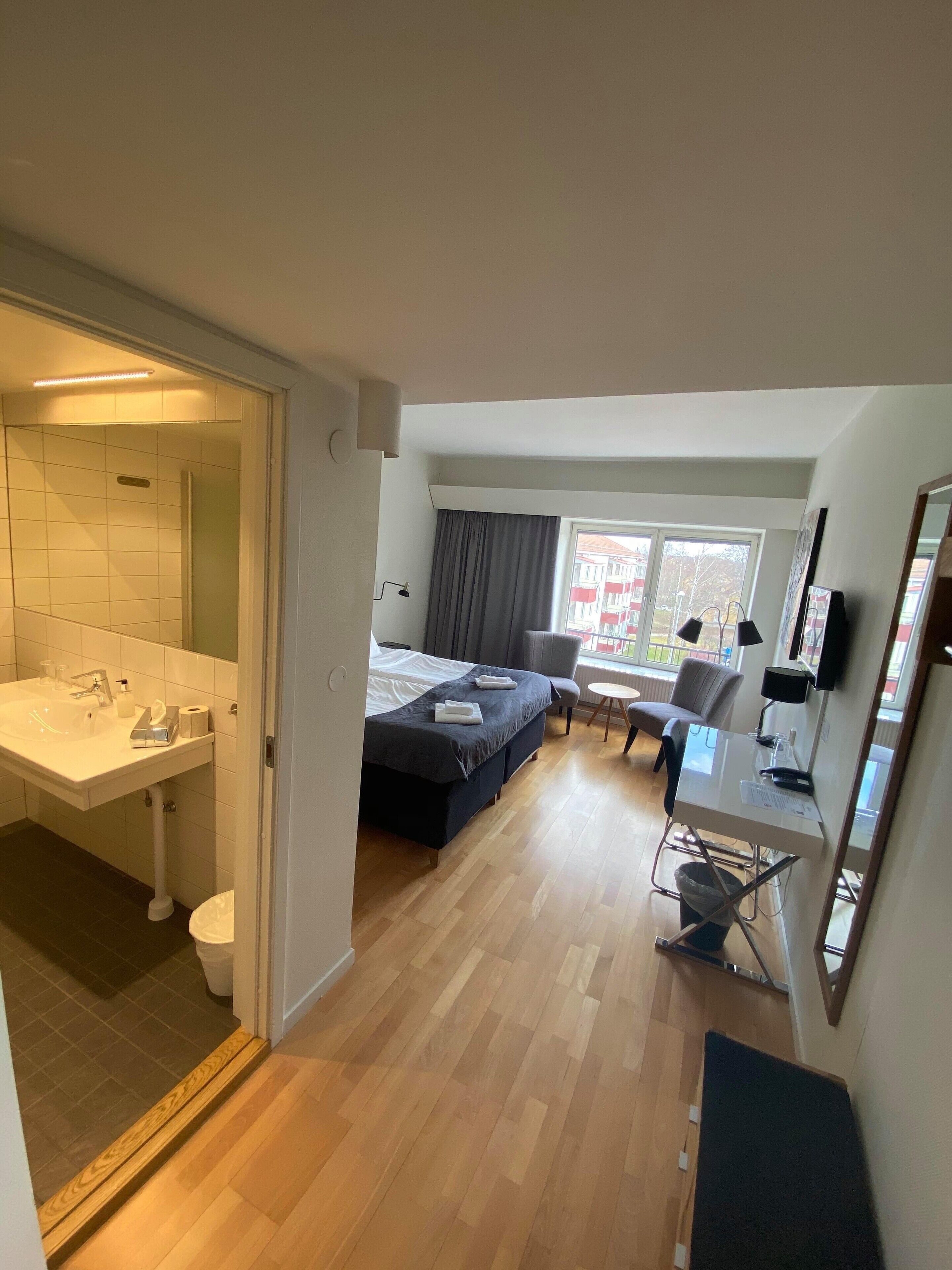 Habitación de hotel con baño, cama, escritorio y ventana.