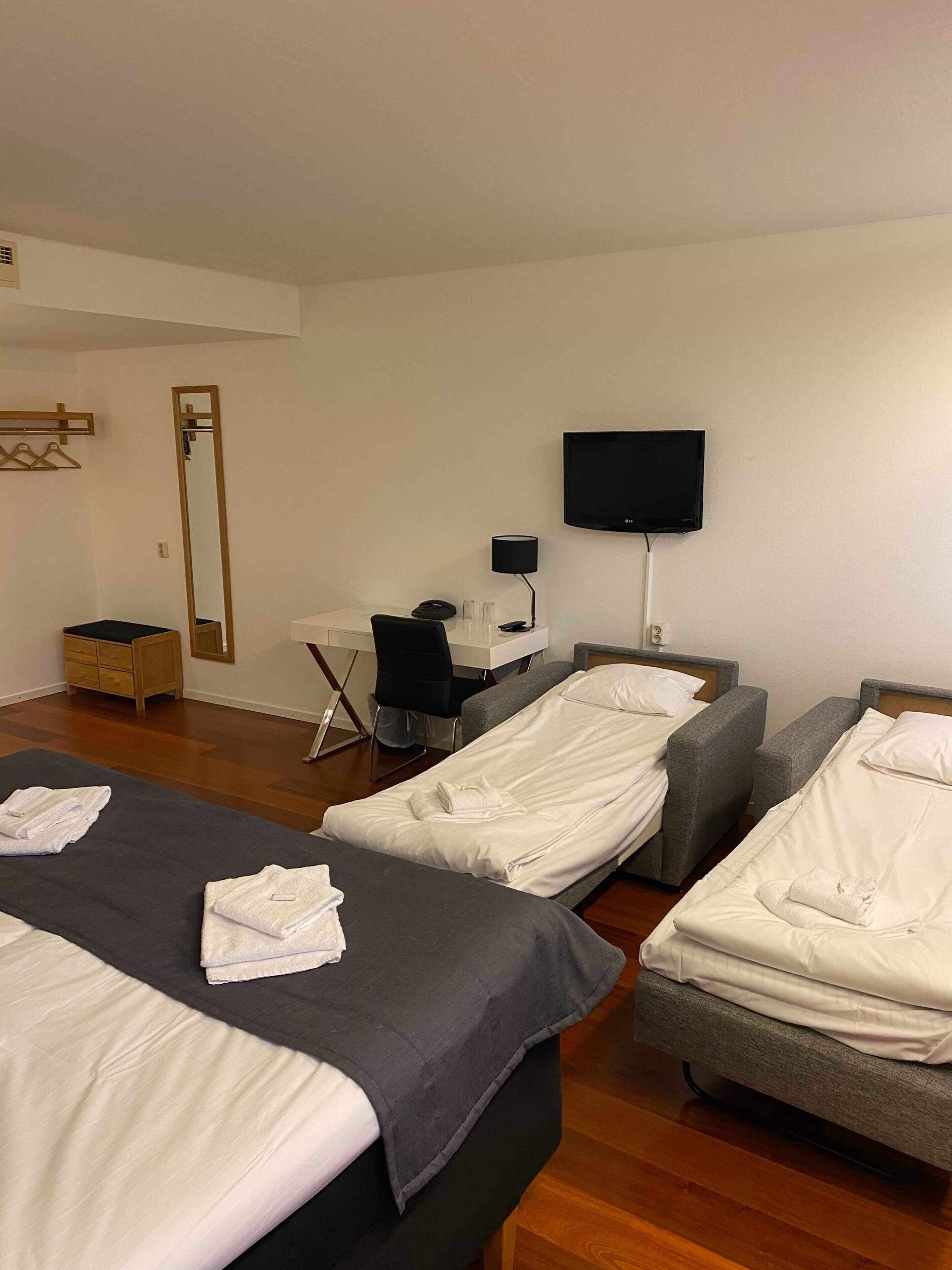 A hotel room with two single beds, a desk with a chair, a TV, and a mirror.