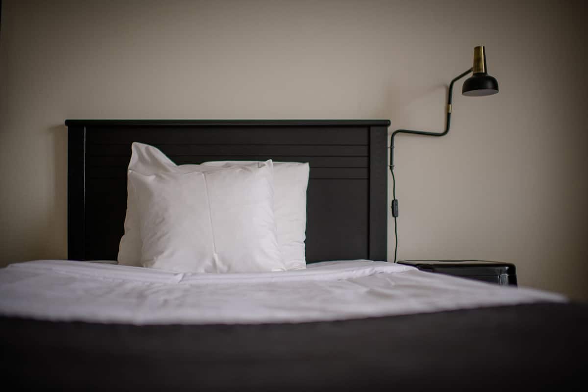 Un lit bien fait, avec une literie blanche, une tête de lit noire et une table de chevet sur laquelle se trouve une lampe.