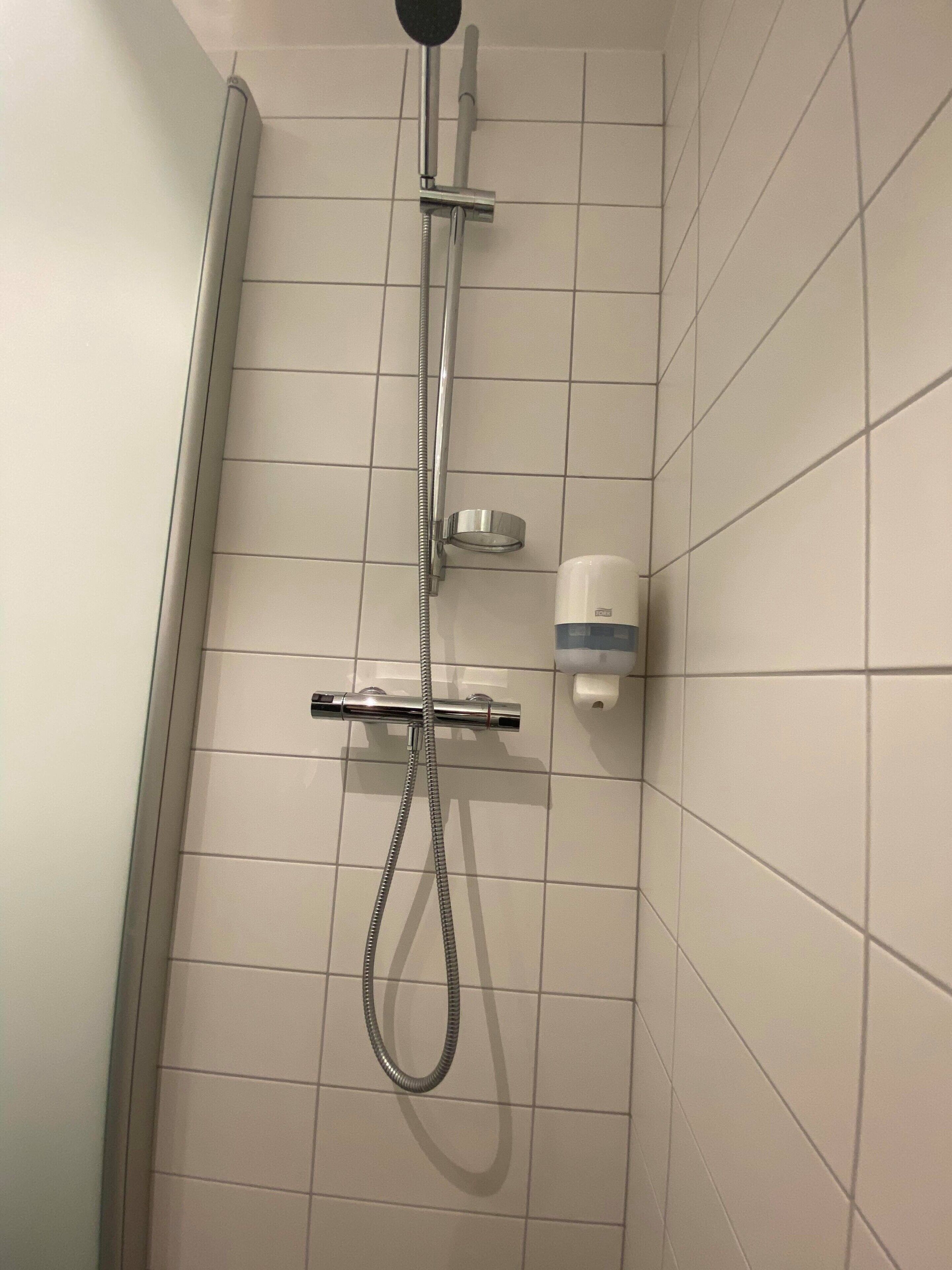 Ducha con cabezal de ducha de mano, manguera de ducha y dispensador de jabón en la pared.