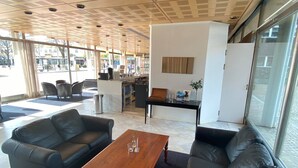 A spacious lobby with leather sofas, a wooden coffee table, and large windows offering views of the street. - Hotell Alfred Nobel (Karlskoga)