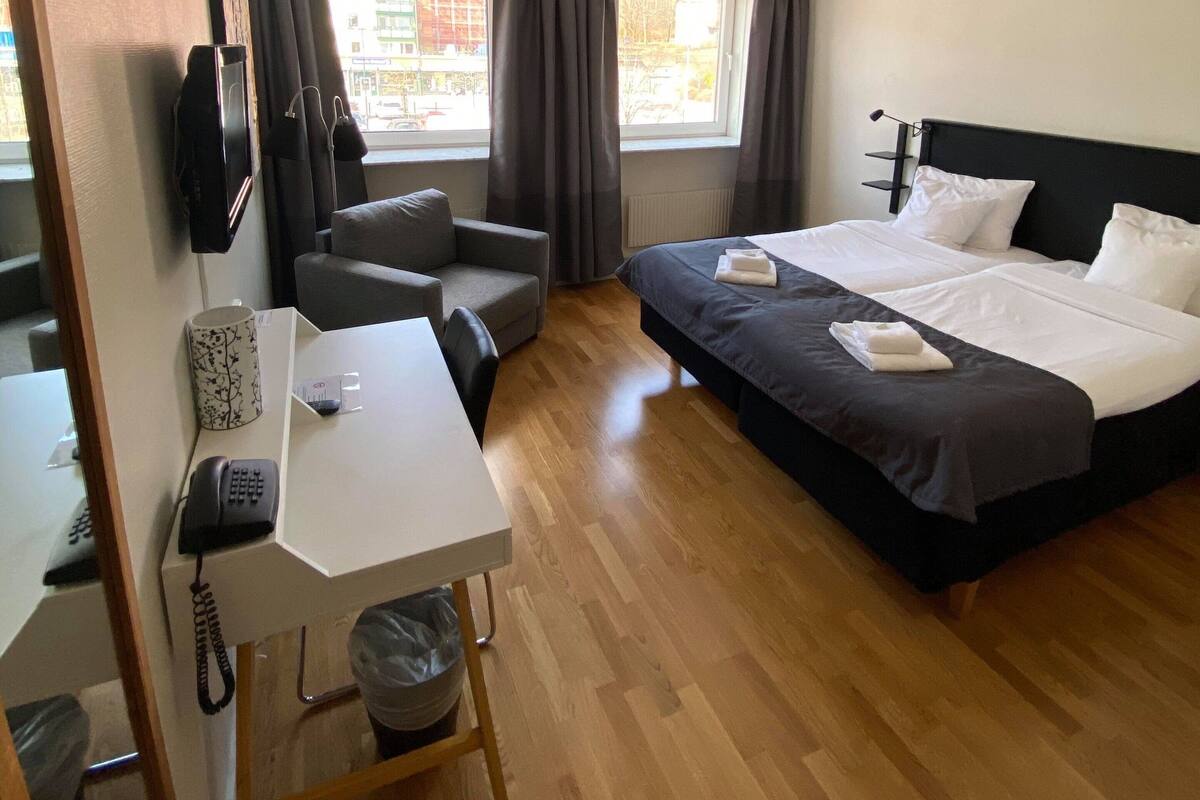 Une chambre d’hôtel avec un lit, un bureau avec un téléphone, une chaise et une fenêtre avec des rideaux.