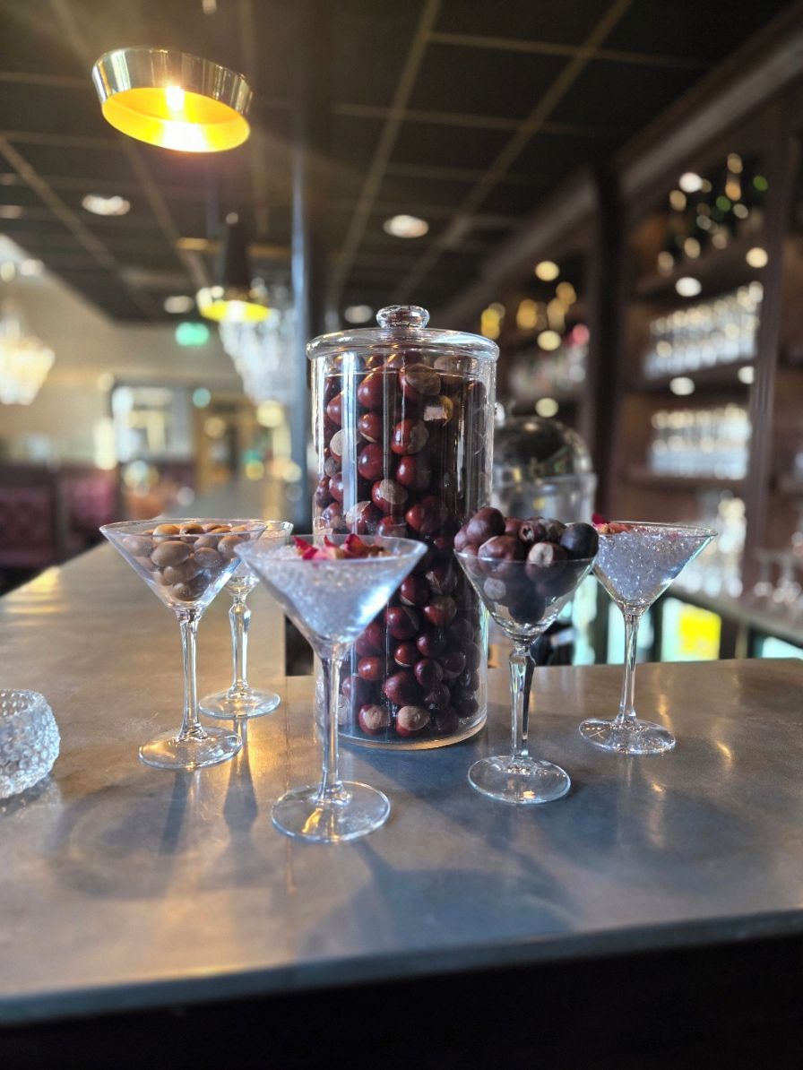 A bar setting with a glass jar filled with nuts and a few martini glasses with nuts on the rim.