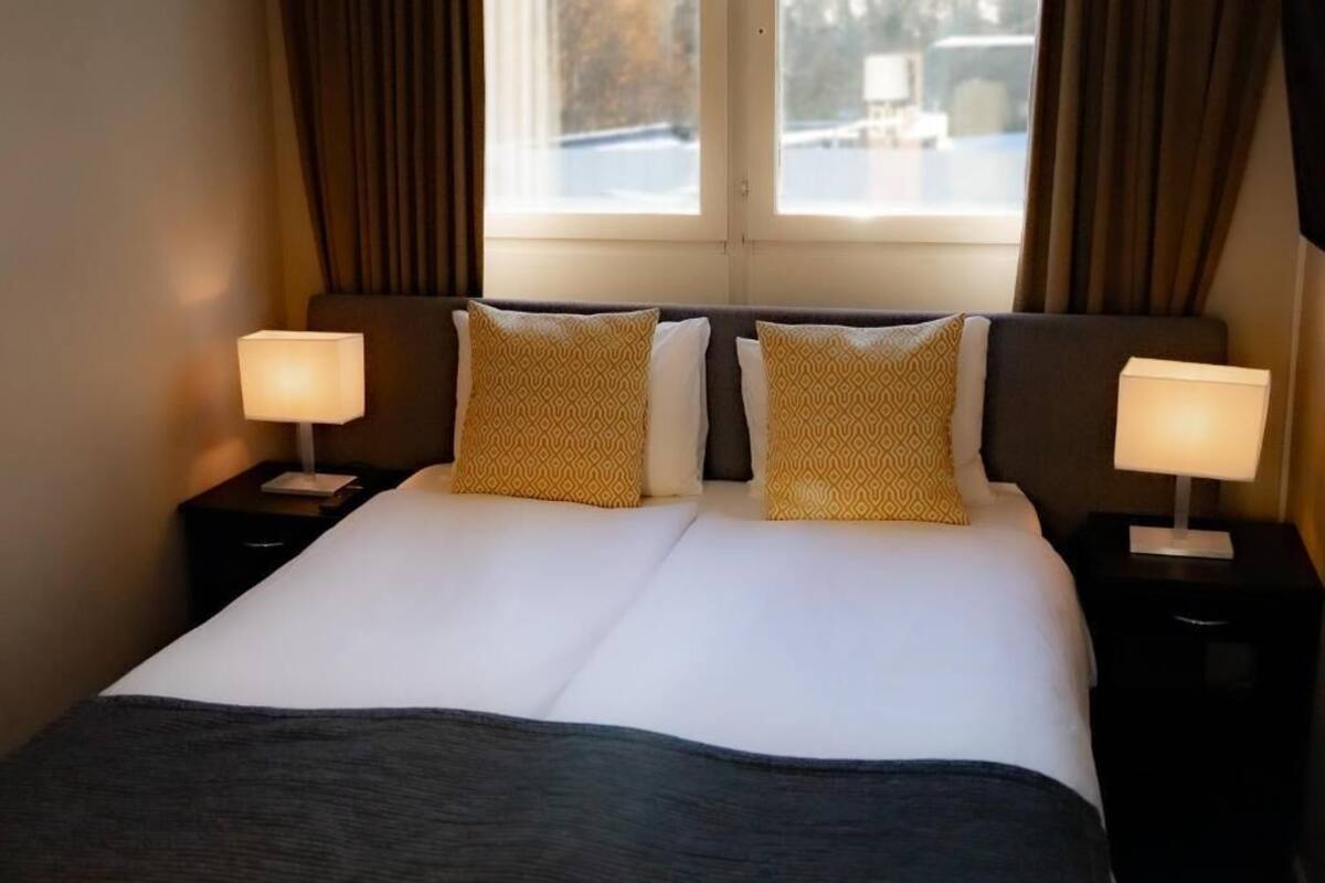 Una cama bien hecha con dos almohadas, un cabecero oscuro y dos lámparas de noche.