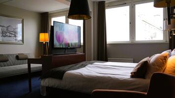 A hotel room with a bed, a TV, a sofa, a lamp, and a window with curtains.
