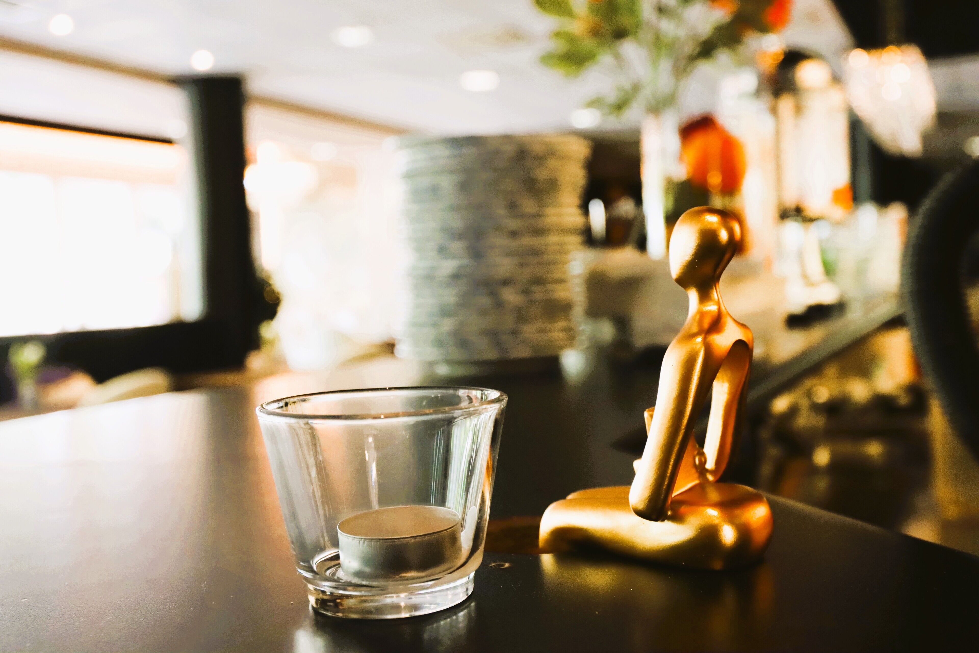 A clear glass candle holder on a dark surface with a golden figurine beside it.