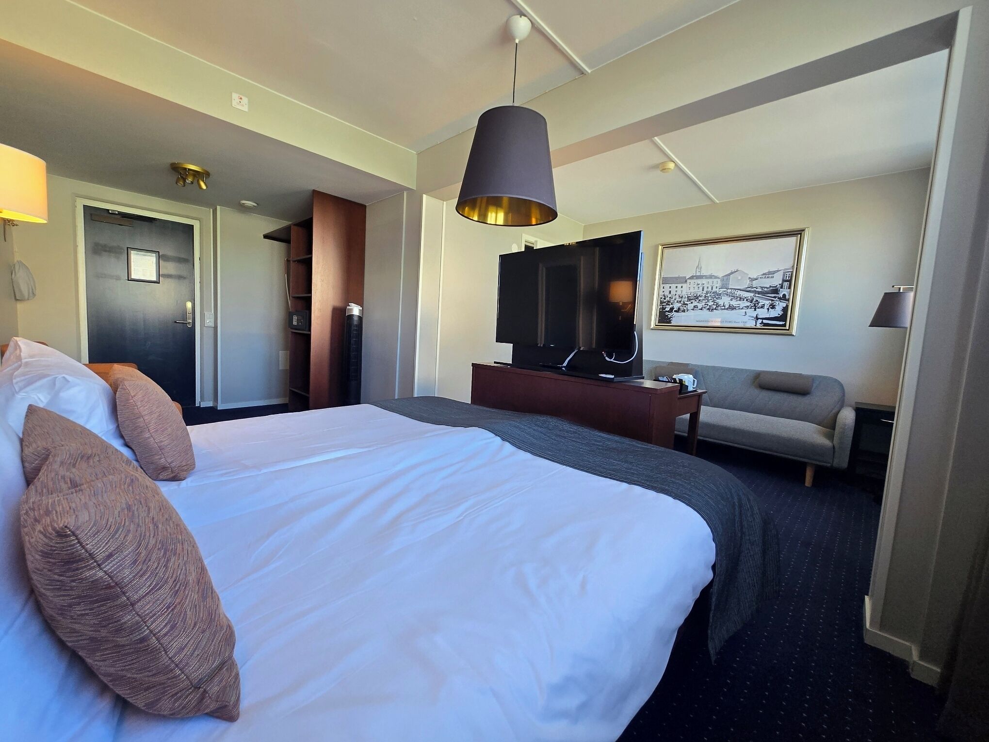 A hotel room with a large bed, a TV, a sofa, and a desk.