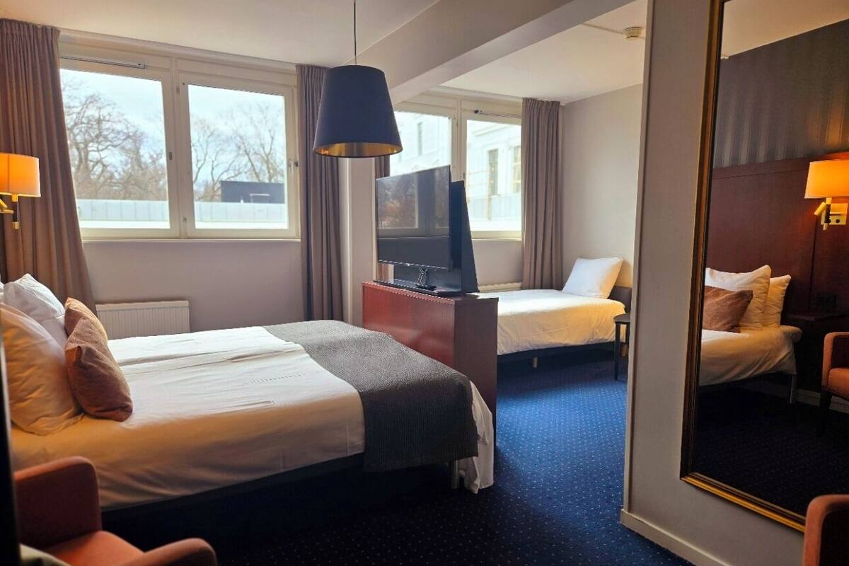 Habitación de hotel con dos camas, televisión, escritorio y un espejo grande.