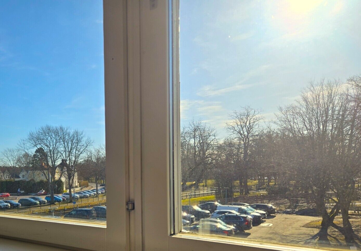 A parking lot with cars and leafless trees, viewed through a window with a door frame.