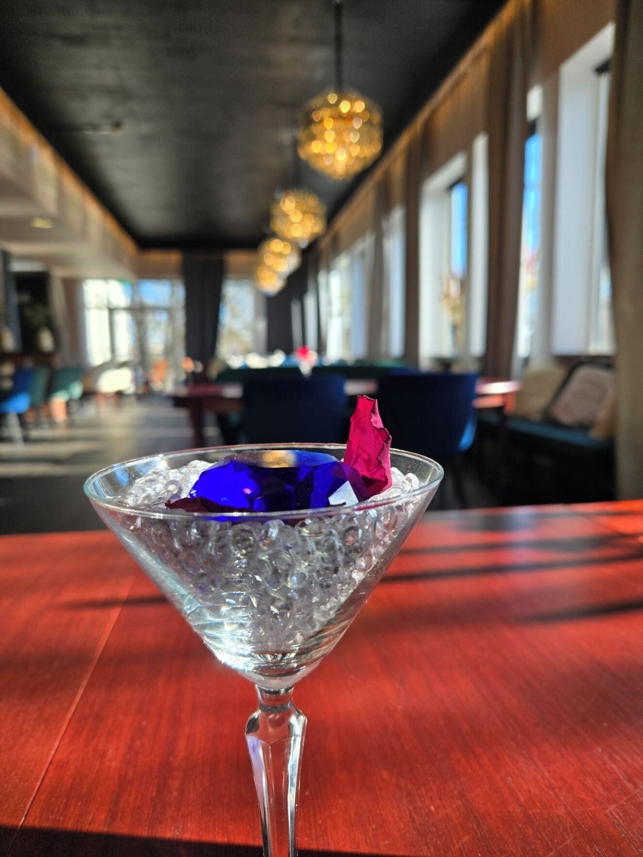 Una copa de martini con hielo y una decoración azul y roja sobre una mesa de madera en un restaurante.