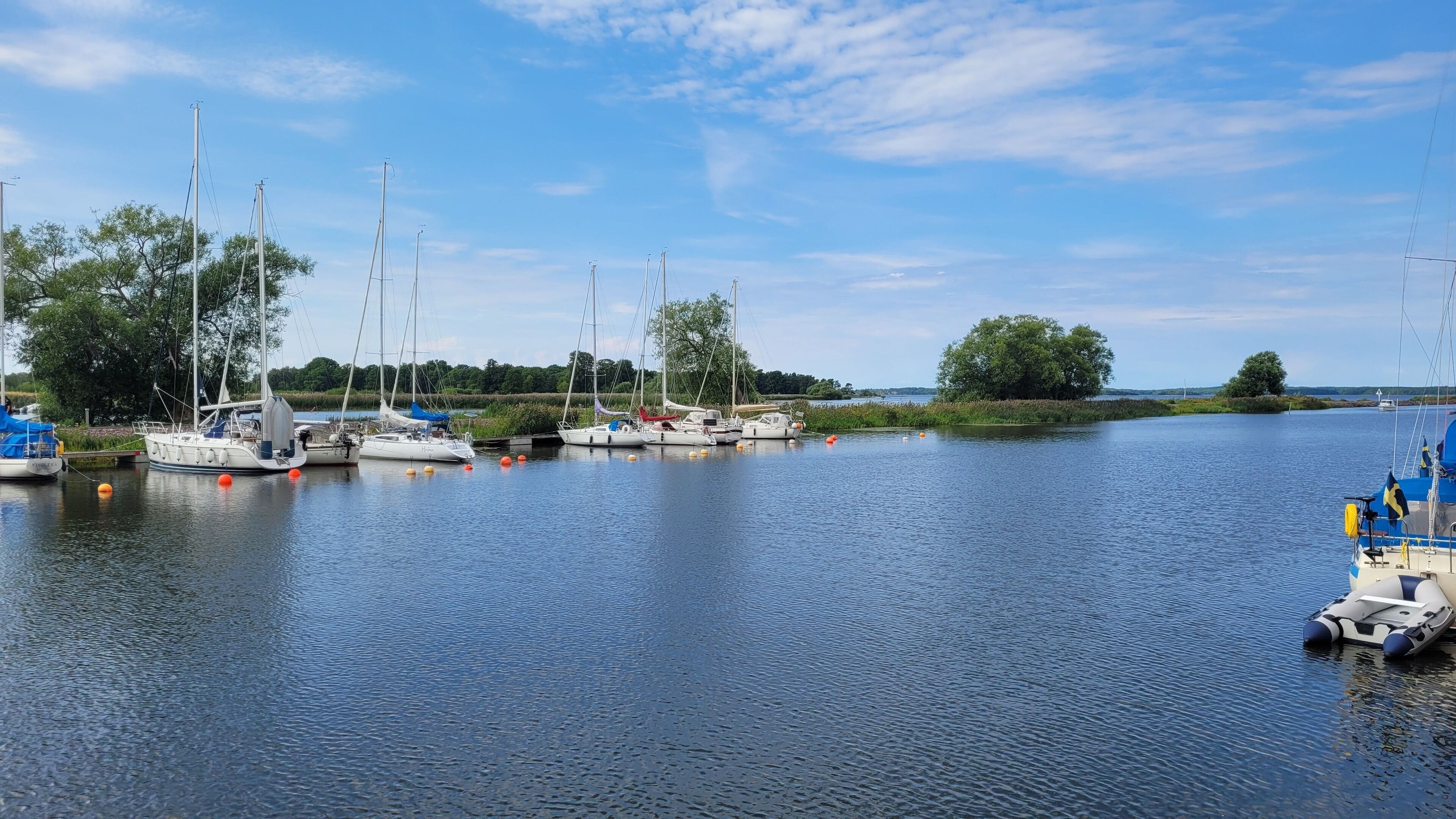 A marina with several sailboats docked, calm water, and a clear sky.