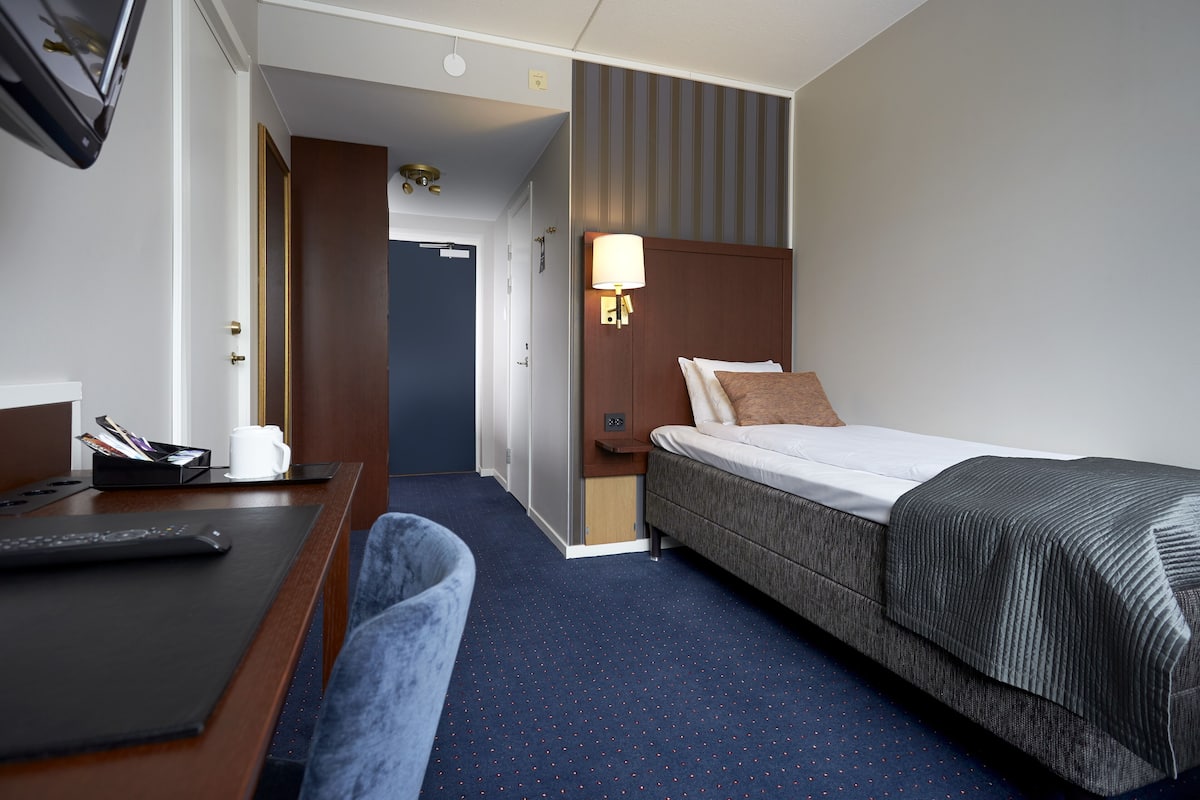Una habitación de hotel con cama, escritorio, silla, lámpara y televisor.