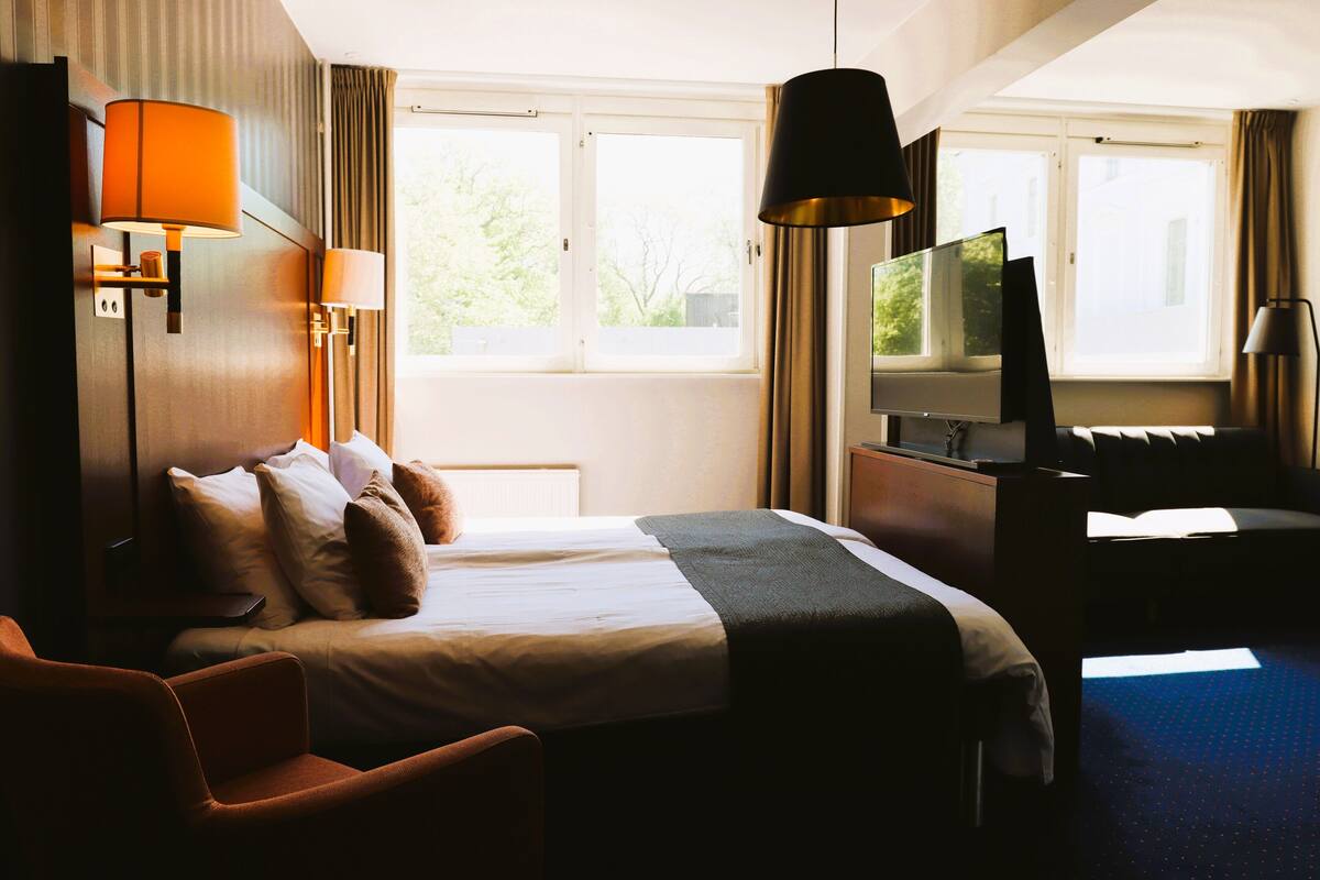 Una habitación de hotel con cama, escritorio, televisor y una silla.