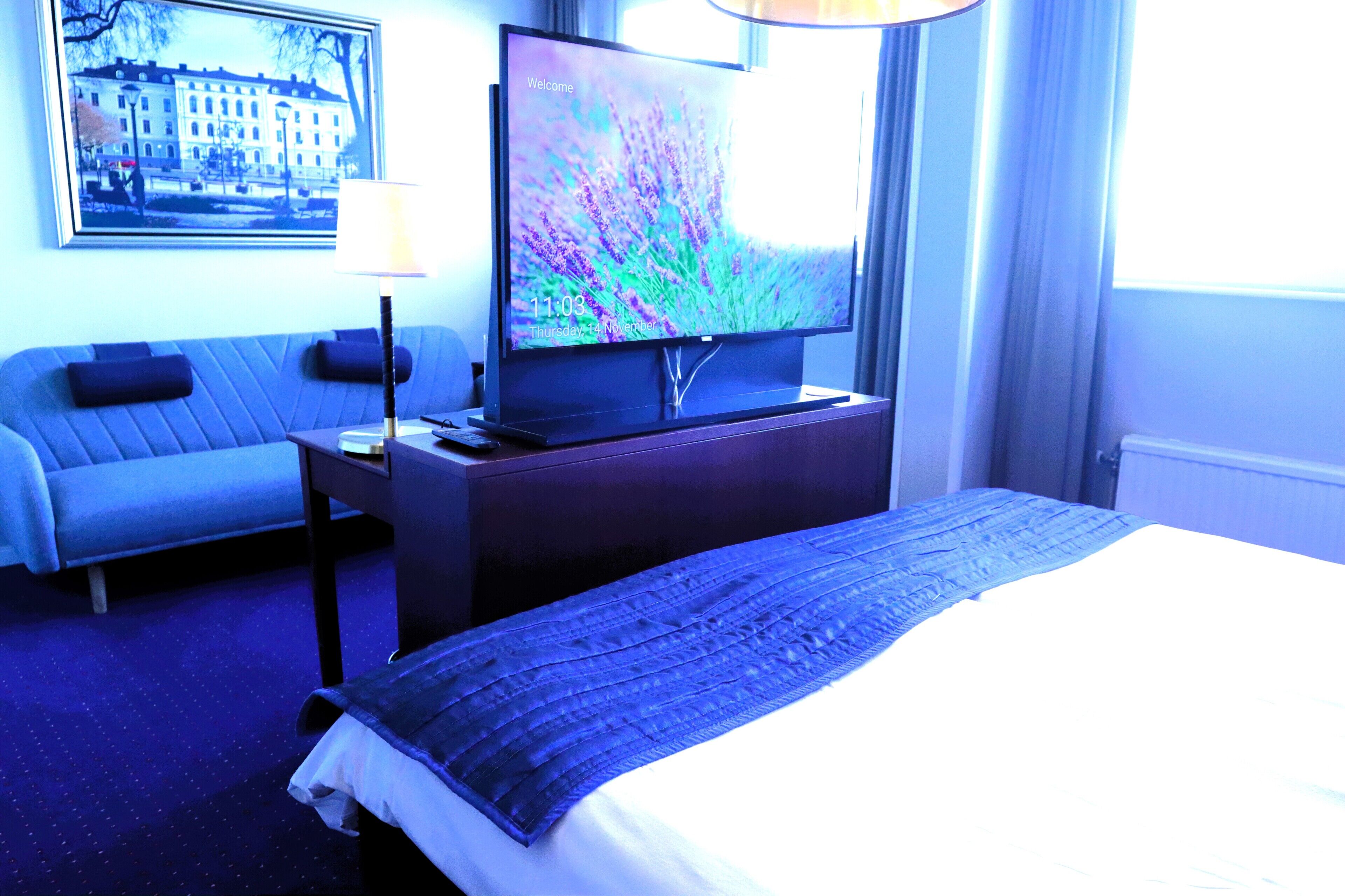 Ett hotellrum med en säng, ett skrivbord med en tv, en soffa och ett fönster med gardiner.