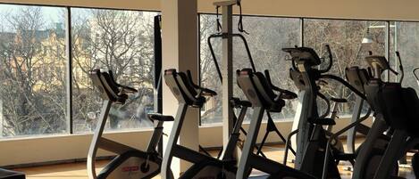 A gym with stationary bikes, large windows, and a view of trees and buildings.