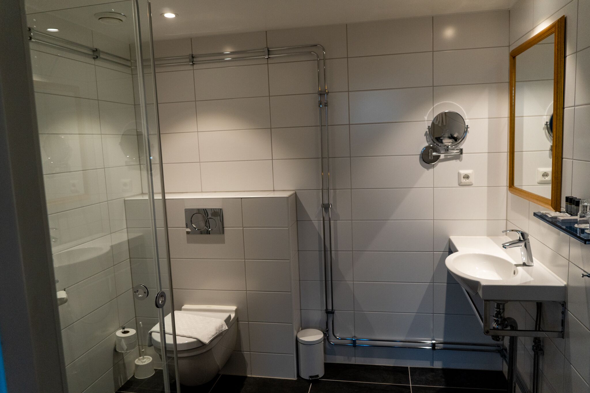 Ett modernt badrum med en dusch som är avskärmad med glasväggar, en vit toalett och ett handfat med en spegel.