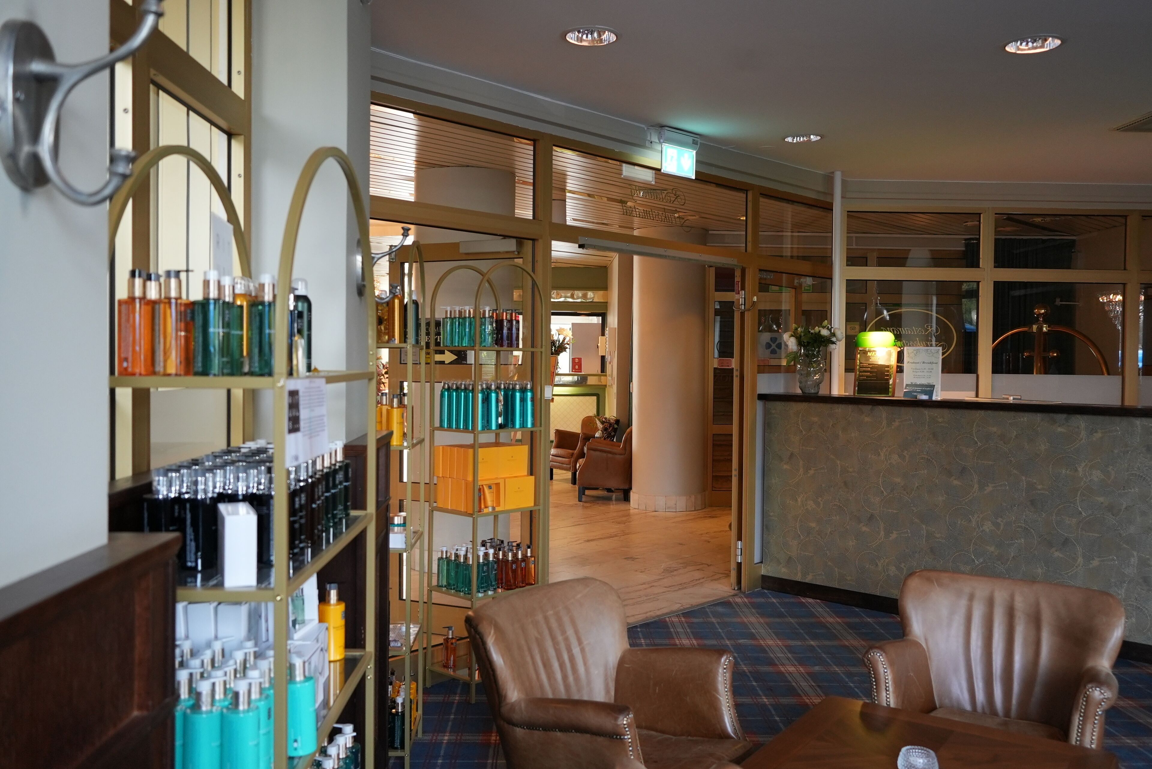A hotel lobby with a bar area, leather armchairs, and shelves of toiletries.