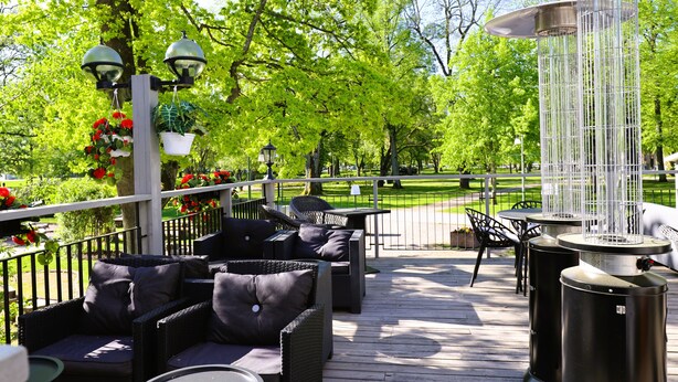 Une terrasse extérieure avec des meubles en osier, un pot suspendu orné de fleurs rouges et un élément décoratif aquatique.